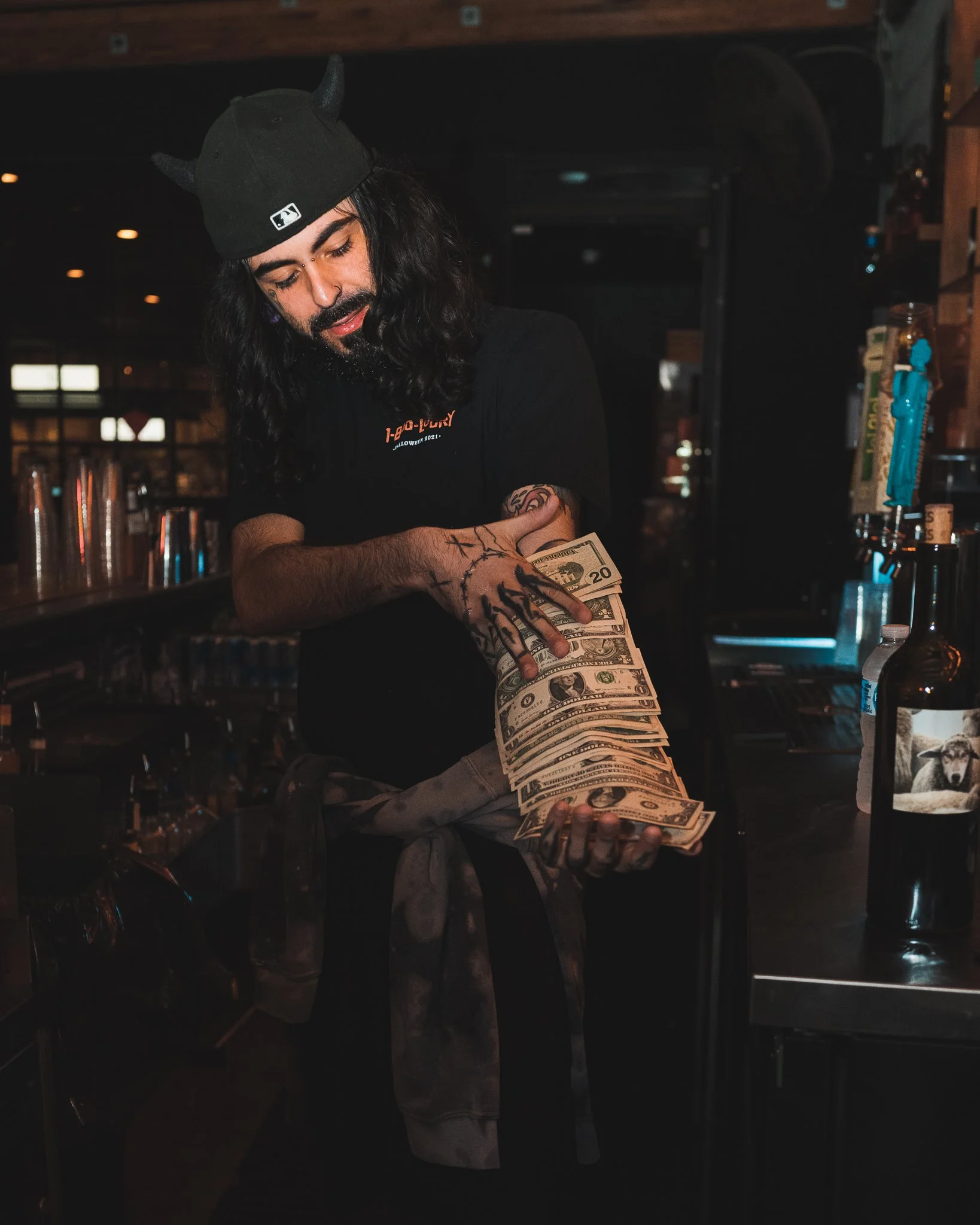 Portrait of TonyDecay in a dimly lit bar environment, holding a large stack of cash.