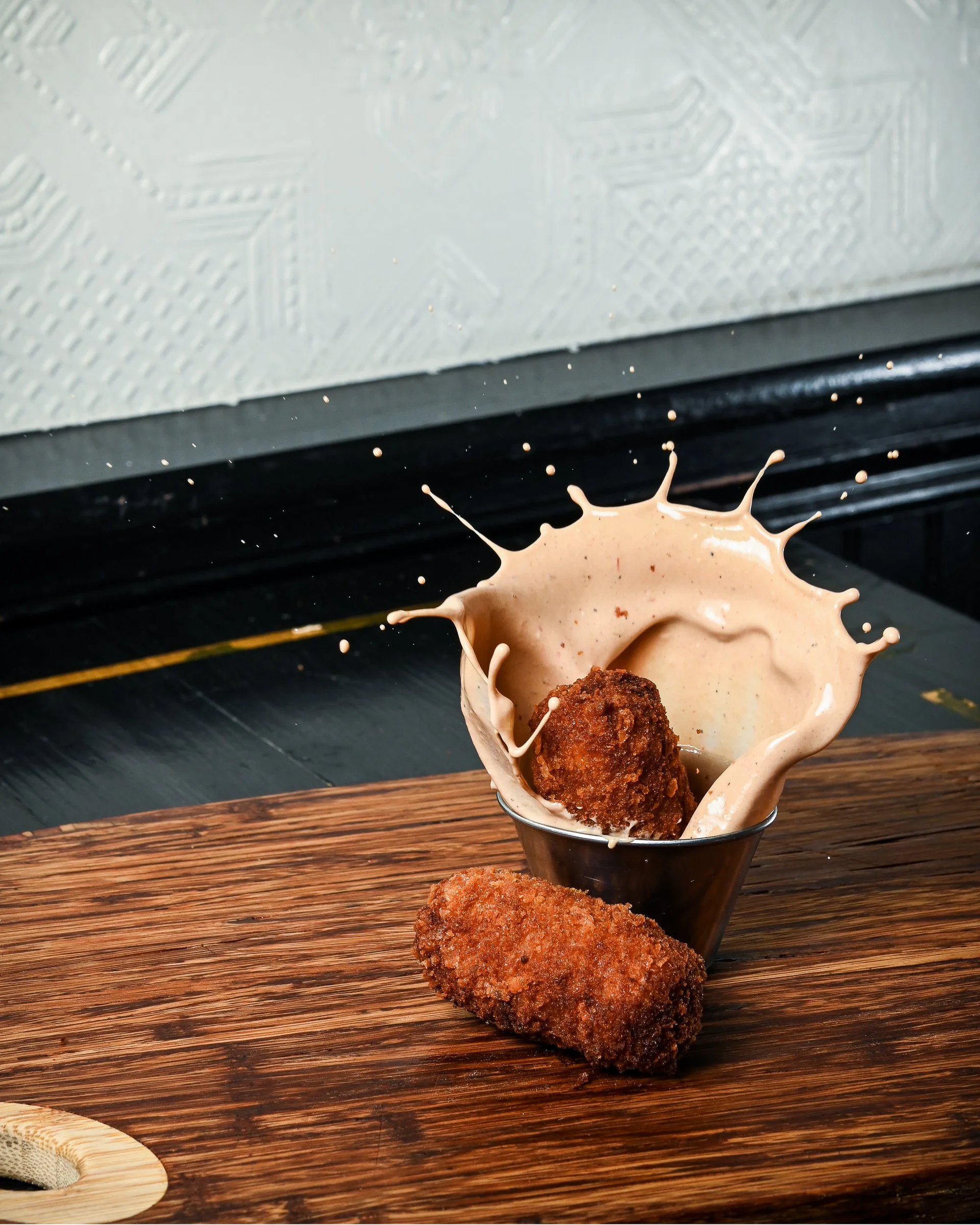 Dramatic food photography of a croqueta splashing into creamy sauce, created by Chef Ken.