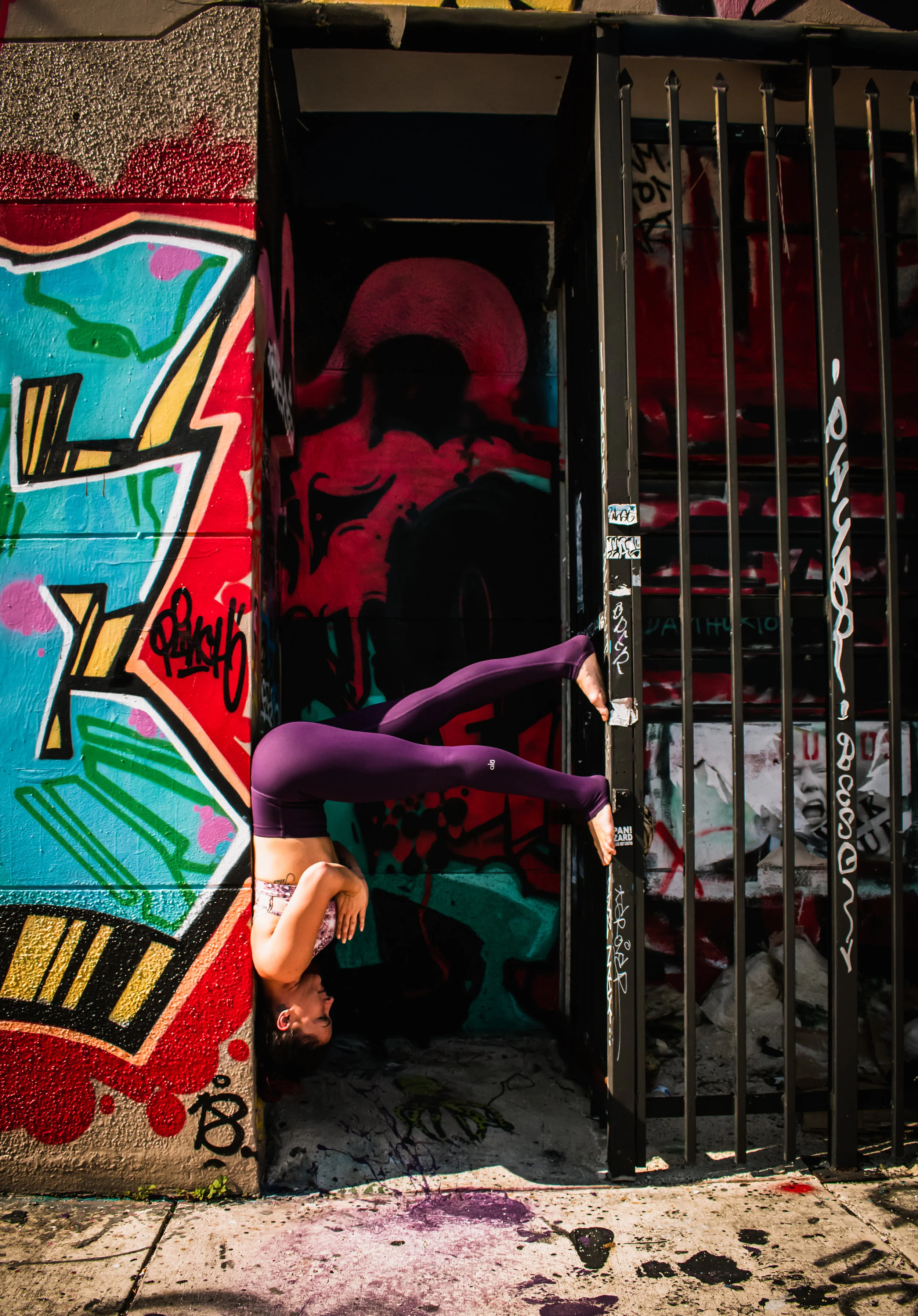 Fitness instructor Lexi Ferra inverted against a graffiti wall in Wynwood, Miami, pressing her feet into the gate for support — yoga pose blending strength, balance and urban street art.