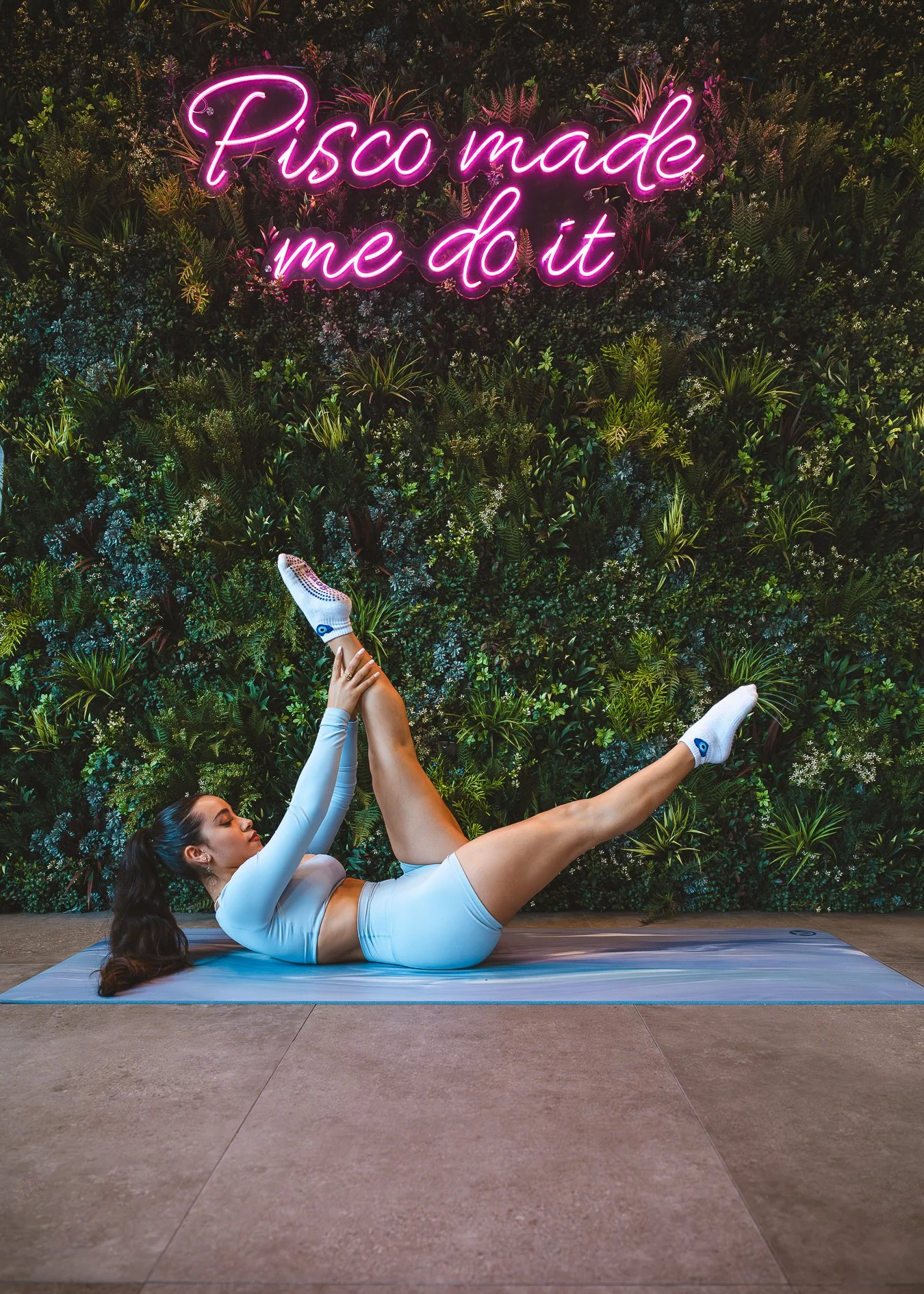 Instructor Sofia Rodriguez demonstrating Pilates under the neon 'Pisco Made Me Do It' sign during her fitness and brunch collaboration with Pisco y Nazca in Coral Gables.