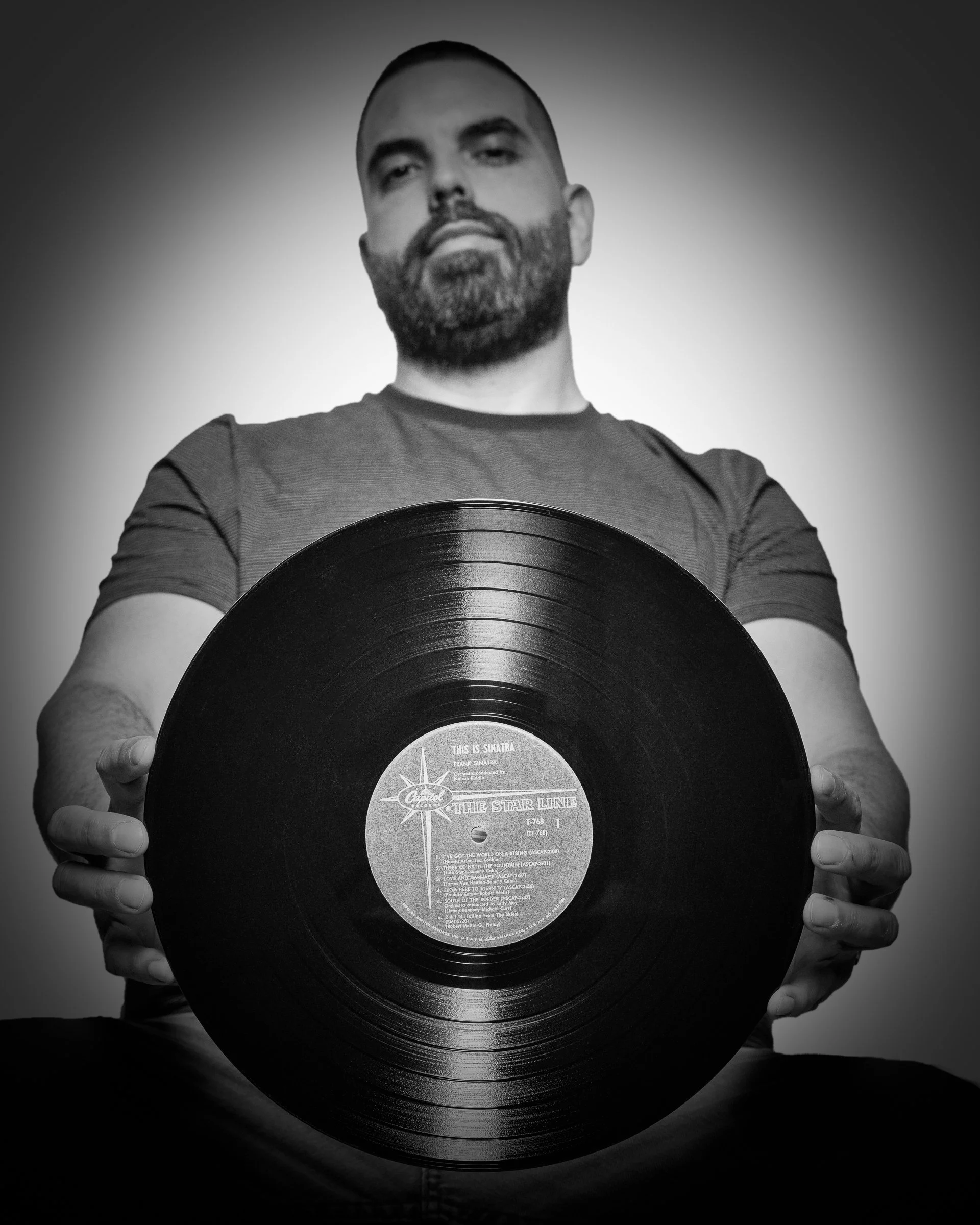 Black-and-white portrait of Eduardo Aleman holding a vinyl record, photographed for portfolio work.
