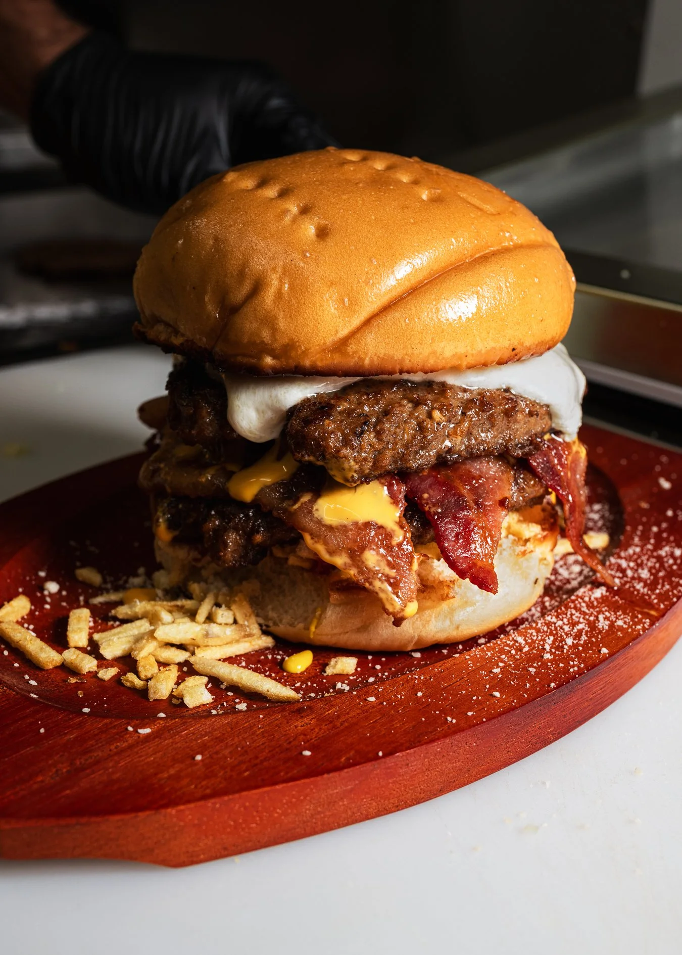 Juicy bacon cheeseburger with melted cheddar, crispy bacon, and potato sticks on a brioche bun, food photography for Woof Hotdog in Miami