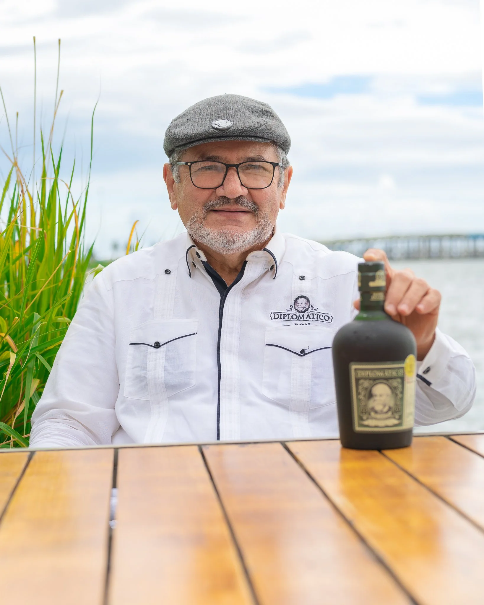 Portrait of Nelson Hernández, master distiller for Diplomático Rum, holding a bottle of Diplomático by the waterfront.