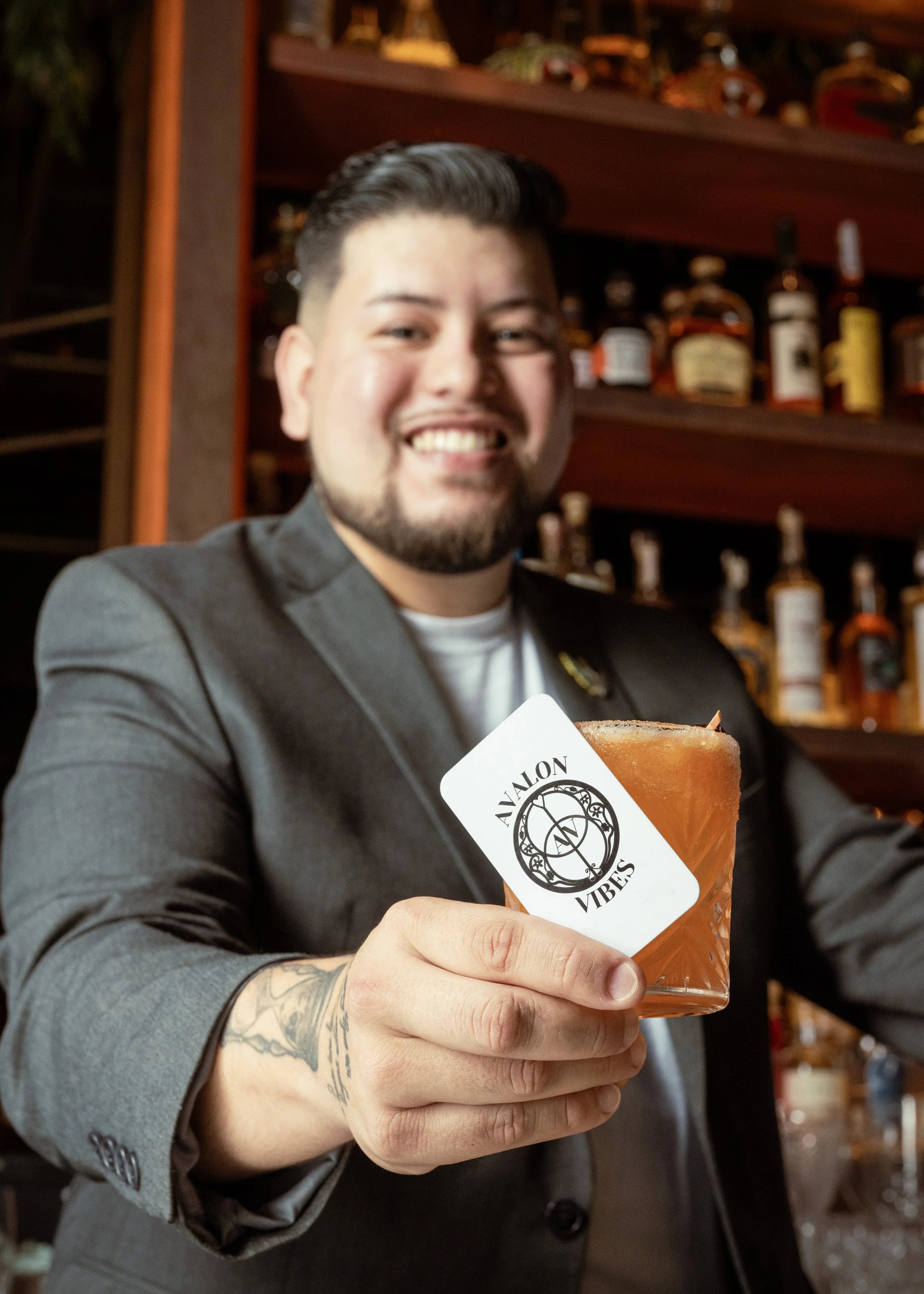 Bartender Fabio Crista smiling while holding a cocktail alongside his Avalon Vibes business card, photographed for his events bartending brand in Miami