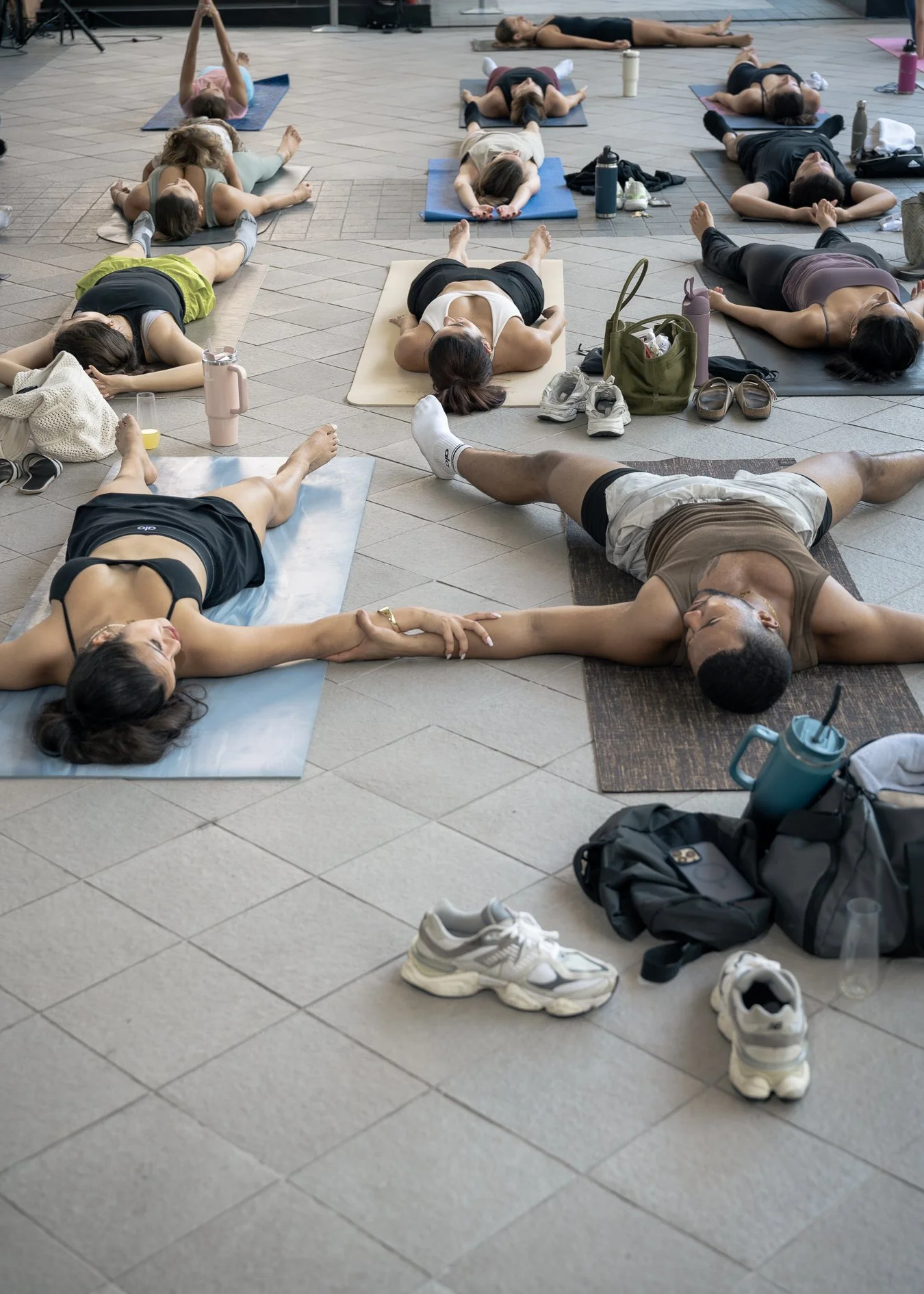 Participants in Savasana (resting pose) holding hands during International Yoga Day at The Plaza Coral Gables, a community wellness event promoting mindfulness and connection.