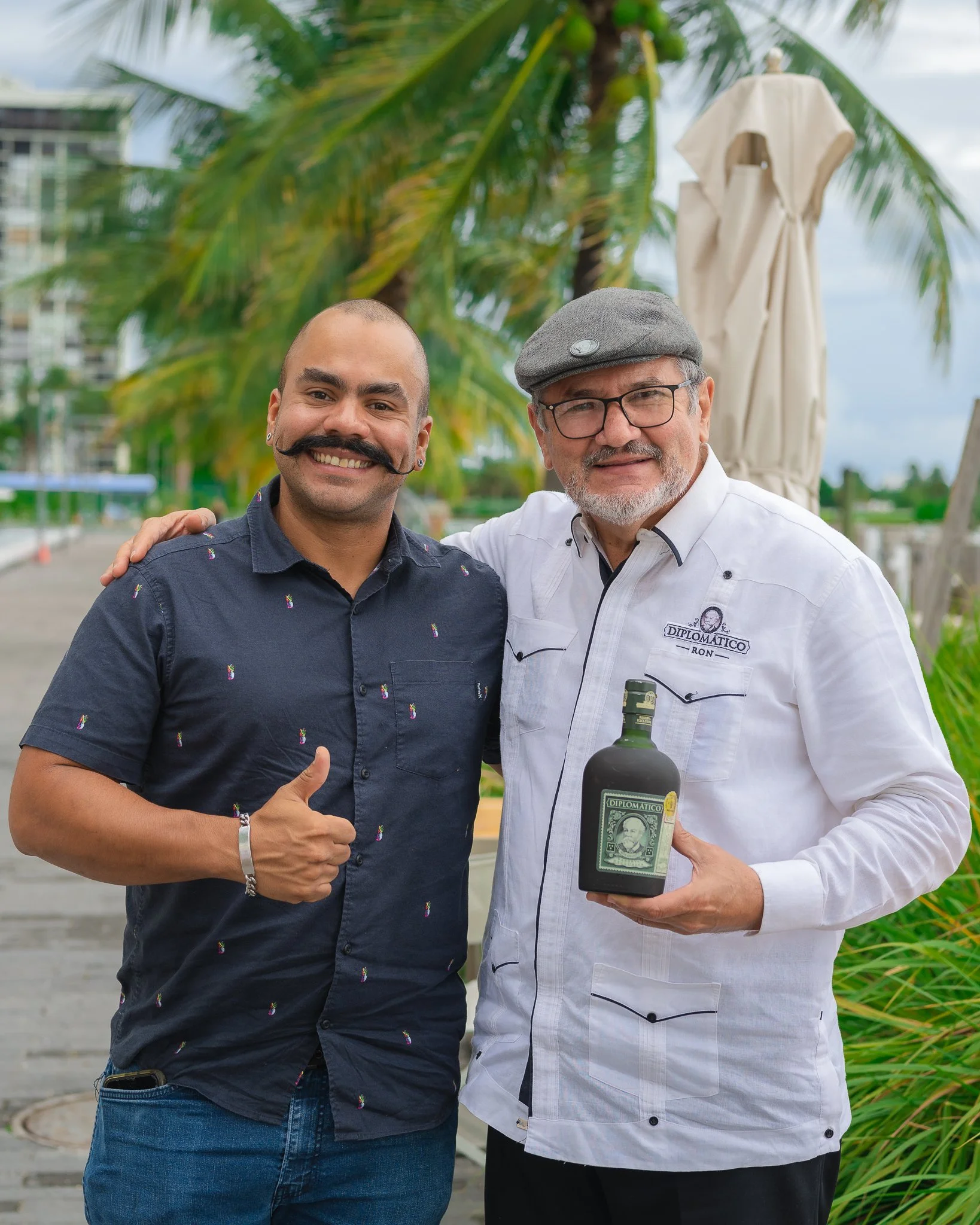 Portrait of Diplomático Rum master distiller Nelson Hernandez holding a bottle of Diplomático alongside bartender Marco Balza at a waterfront event at Amara at Paraiso in Edgewater.