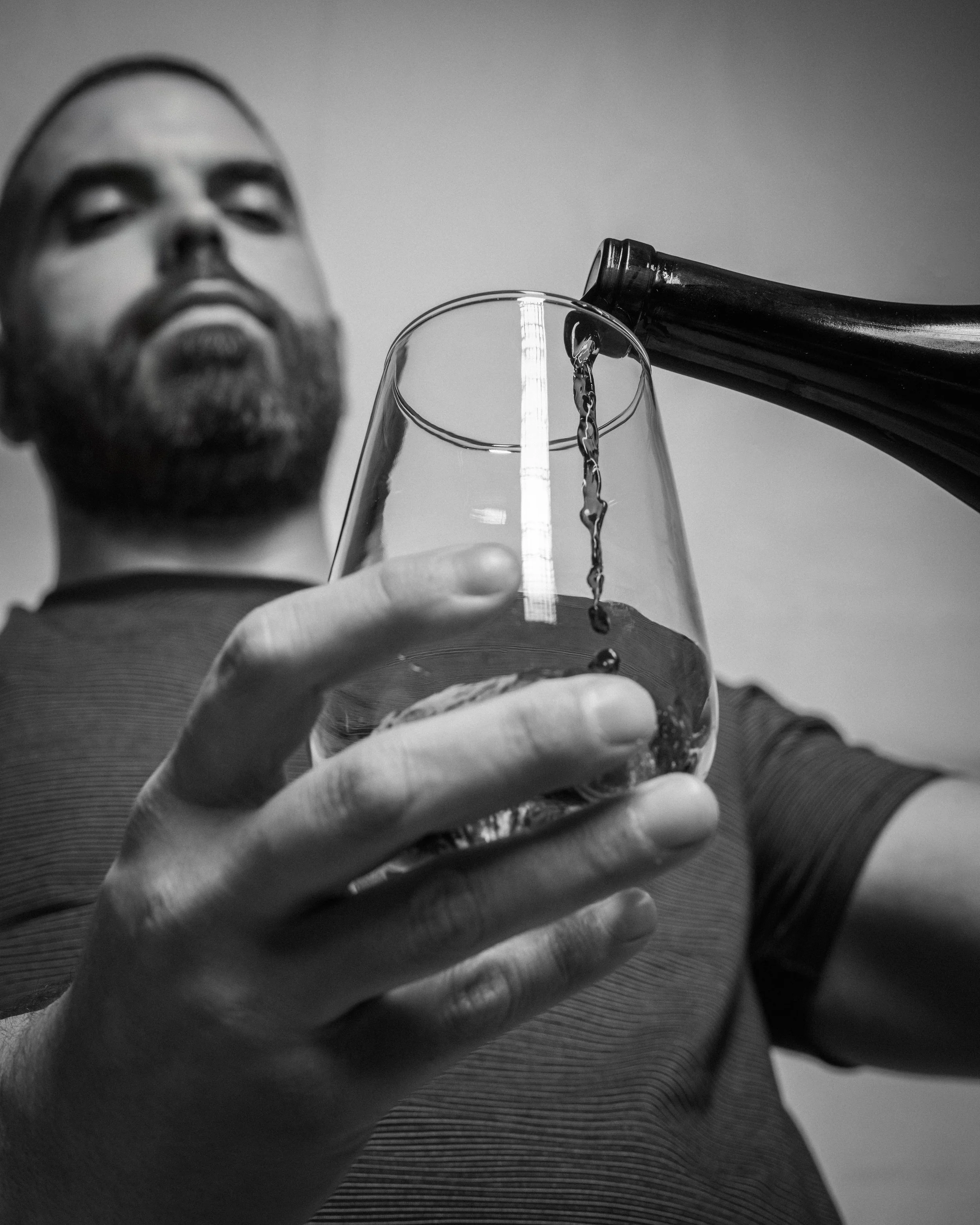 Black-and-white portrait of Eduardo Aleman pouring wine into a glass, photographed for portfolio work.