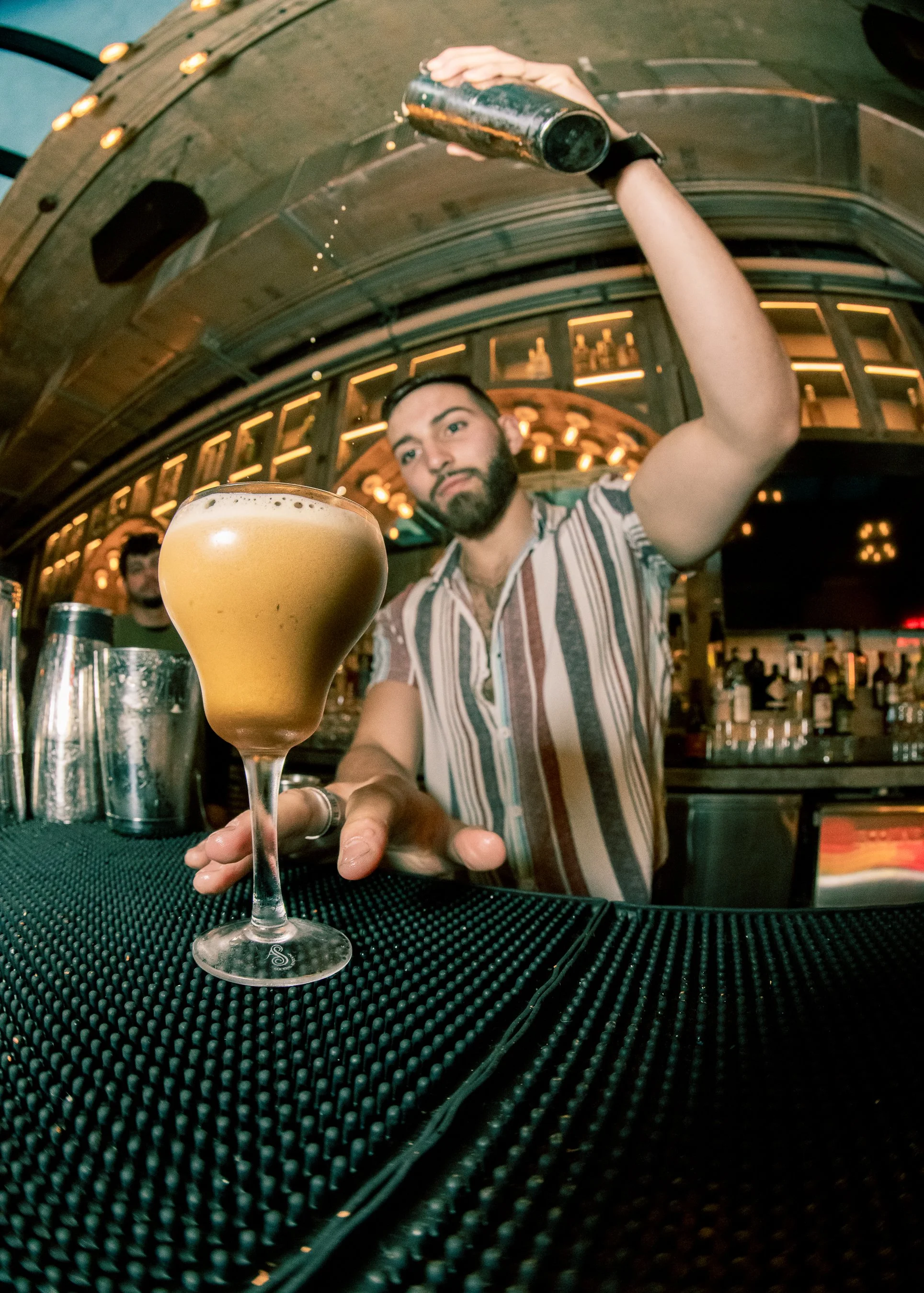 Bartender Alejandro Gil pouring a cocktail with a high pour technique behind the bar at Bodega Taqueria y Tequila in Coconut Grove, photographed for his social media.