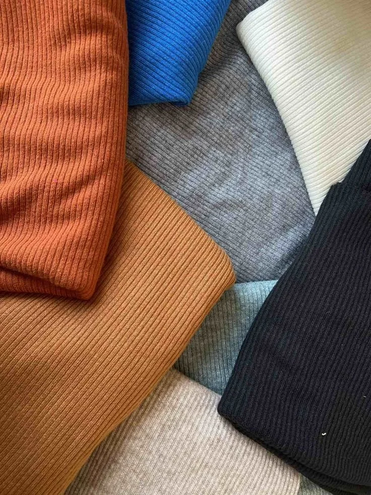 A collection of folded ribbed fabric in various colors, including orange, blue, beige, gray, black, white, and light green.