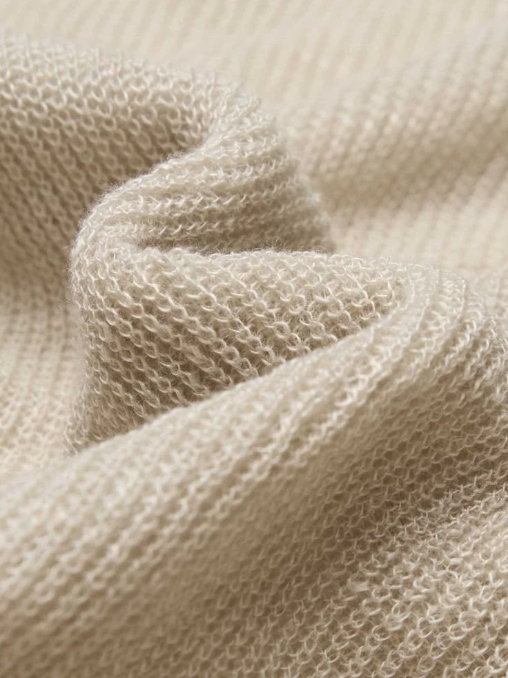 Close-up of beige, textured fabric with a knitted pattern and soft folds.