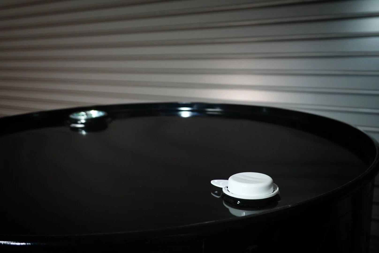 Close-up of a black barrel with a white lid, set against a gray, horizontally ridged metal background.