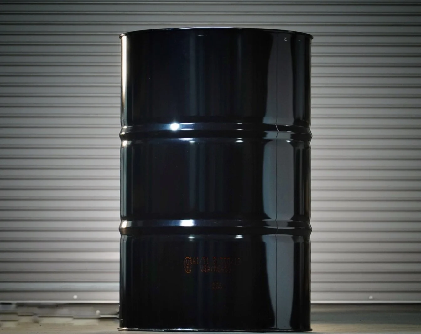 Three black oil drums stacked on a concrete surface with a metallic roll-up door in the background.