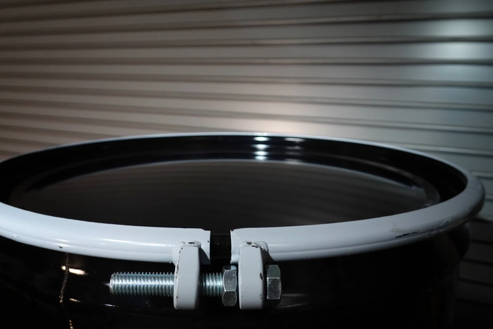 Close-up of a stainless steel ring clamp with white and silver bolts in front of a metallic garage door.