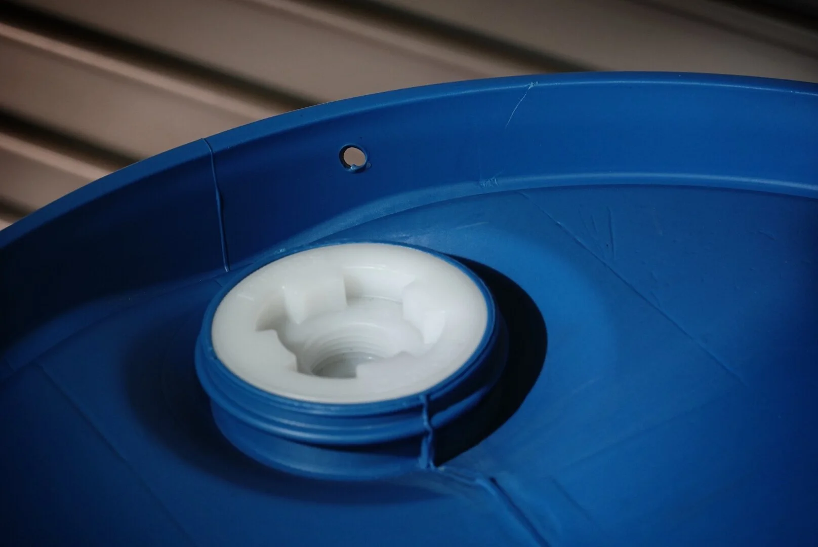 Close-up of a blue plastic barrel with a white plastic bung or cap in the opening.