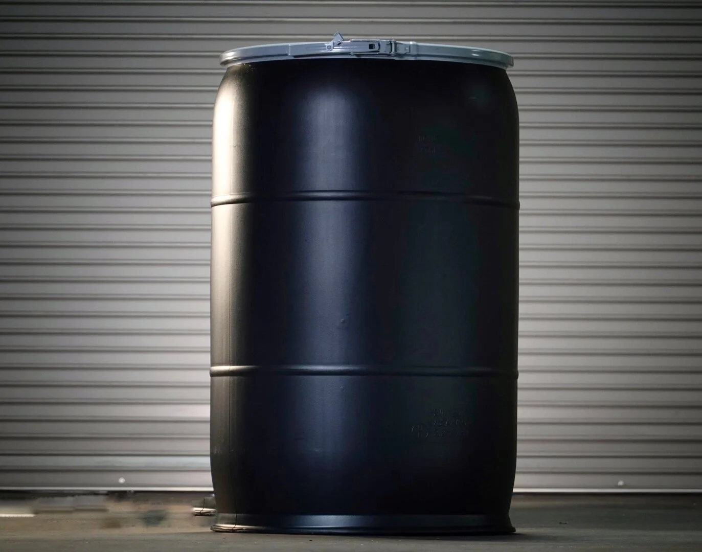 A black industrial barrel standing upright in front of a metal garage door.