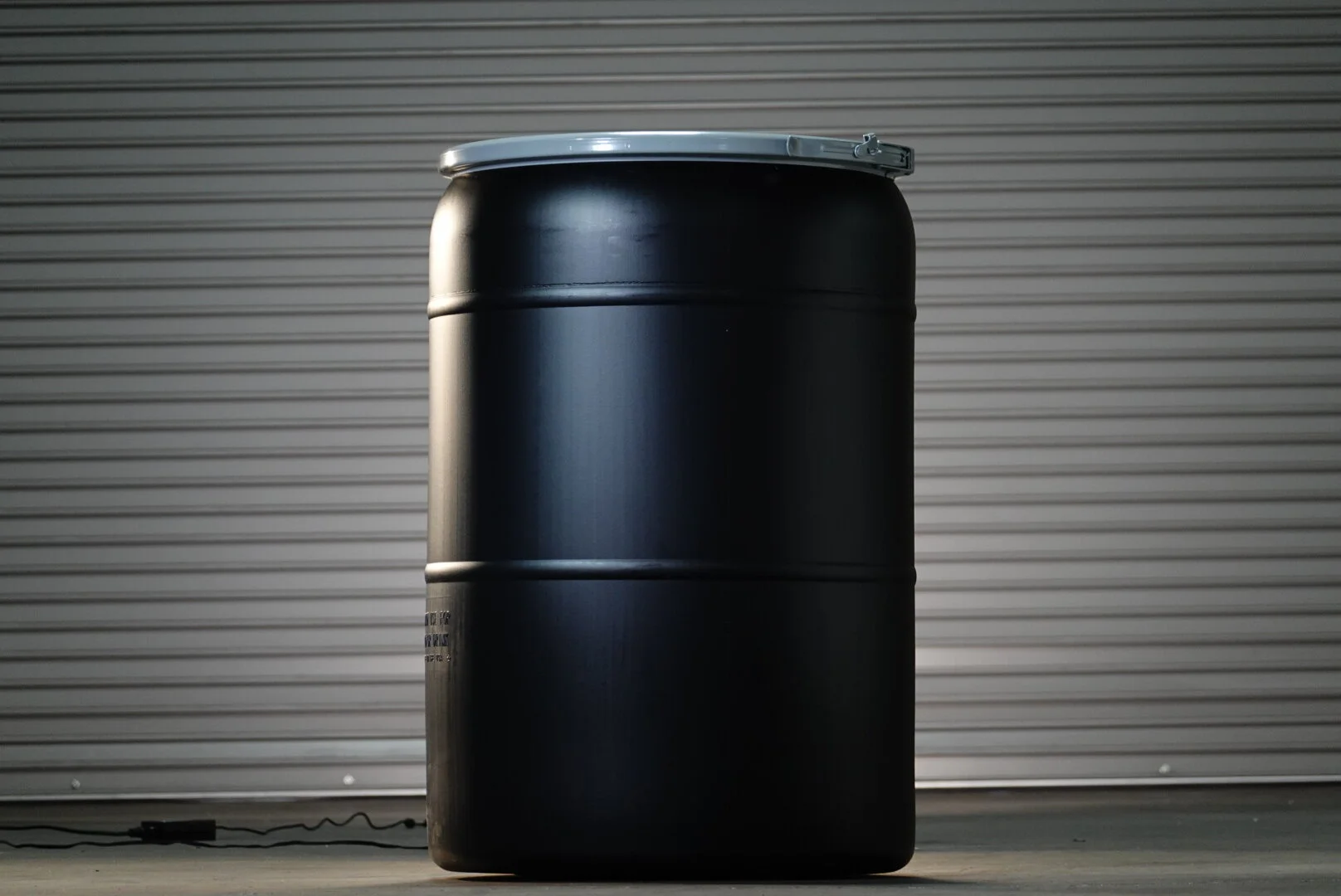A large black metallic barrel with a silver lid set against a metal roll-up door.