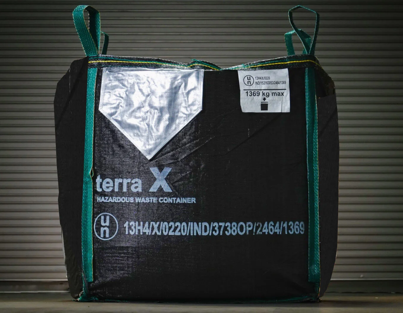 A black hazardous waste container with teal handles and accents, marked with the label 'terra X' and safety information, placed against a corrugated metal background.