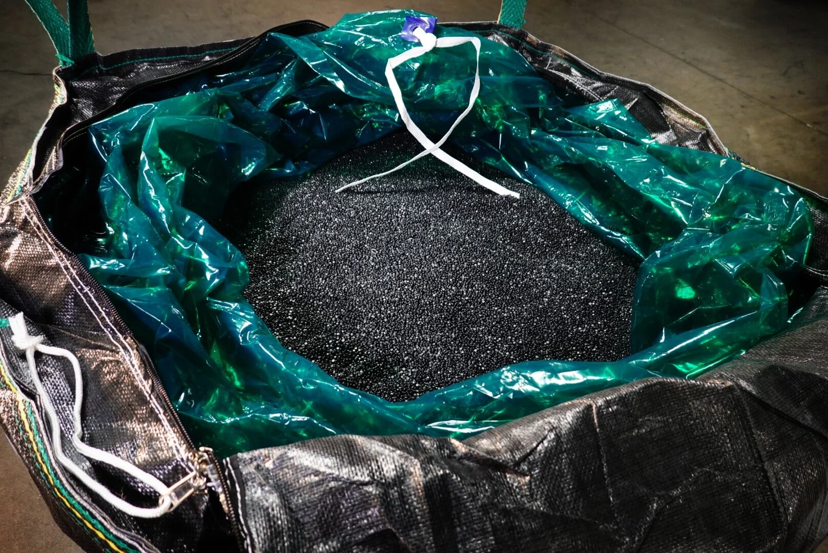 A large black bag contains a green plastic liner filled with small black granules.