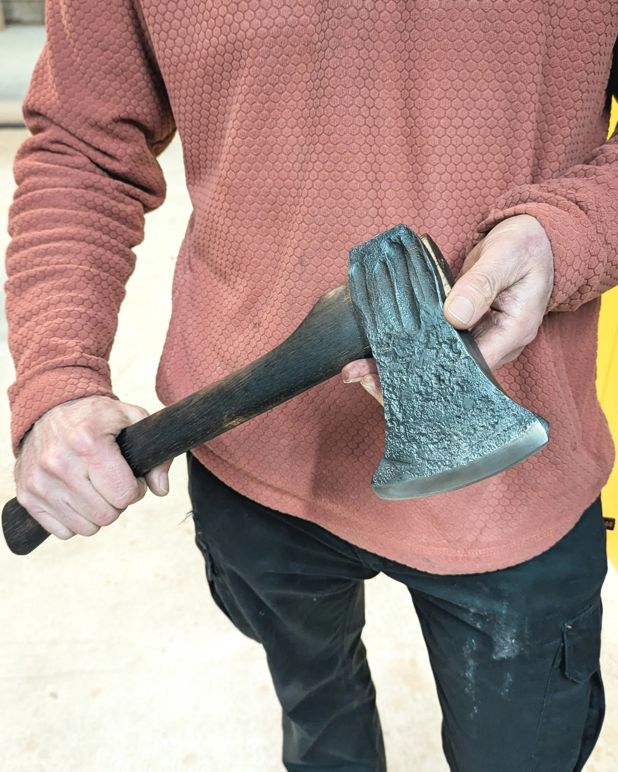 Close-up of a student’s hand gripping a custom axe, showing the raised grain of the flame-treated handle and the polished, razor-sharp edge of the blade.