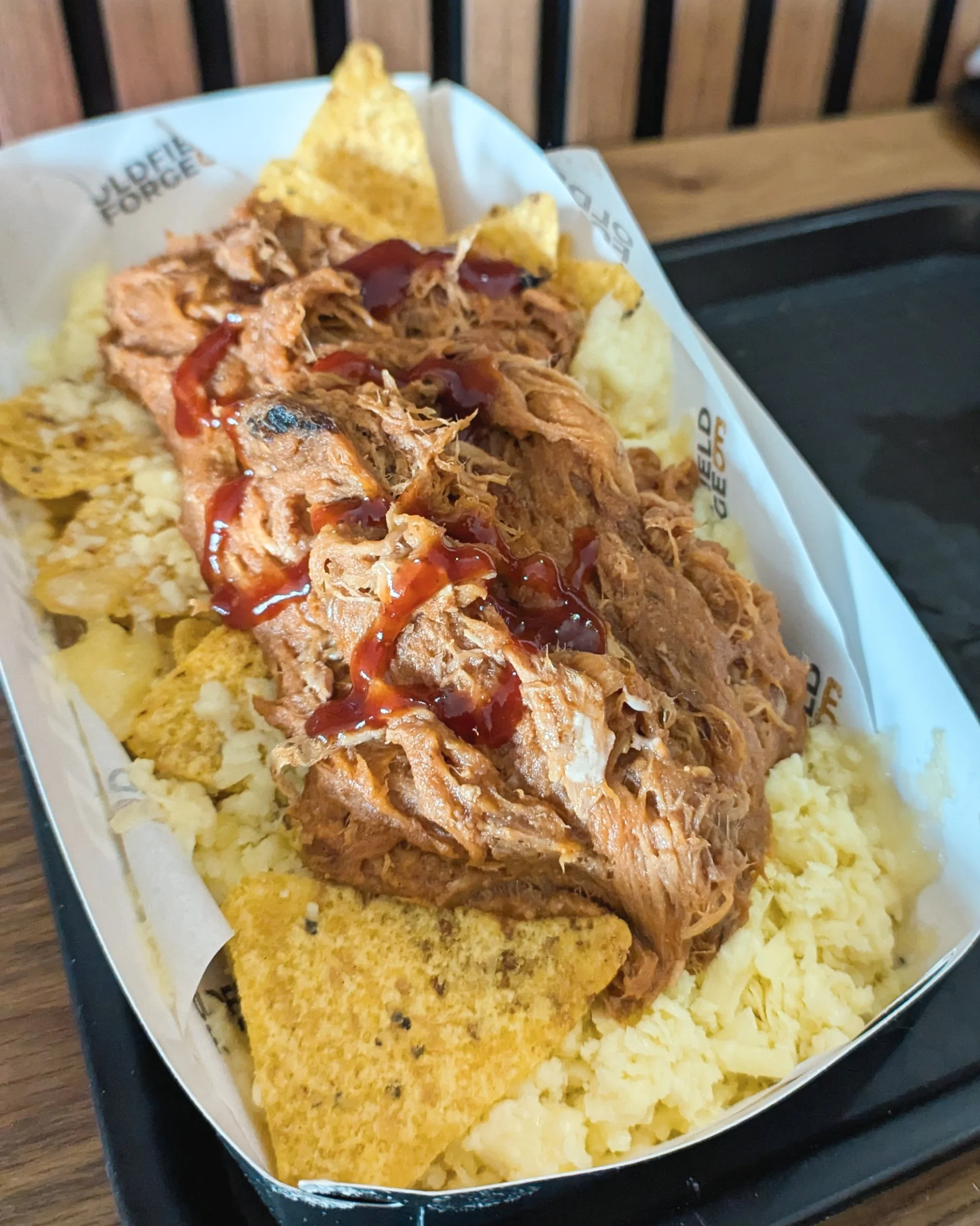 A tray of loaded nachos topped with pulled pork, melted cheese, served during a lunch break at an Oldfield Forge blacksmithing experience day.