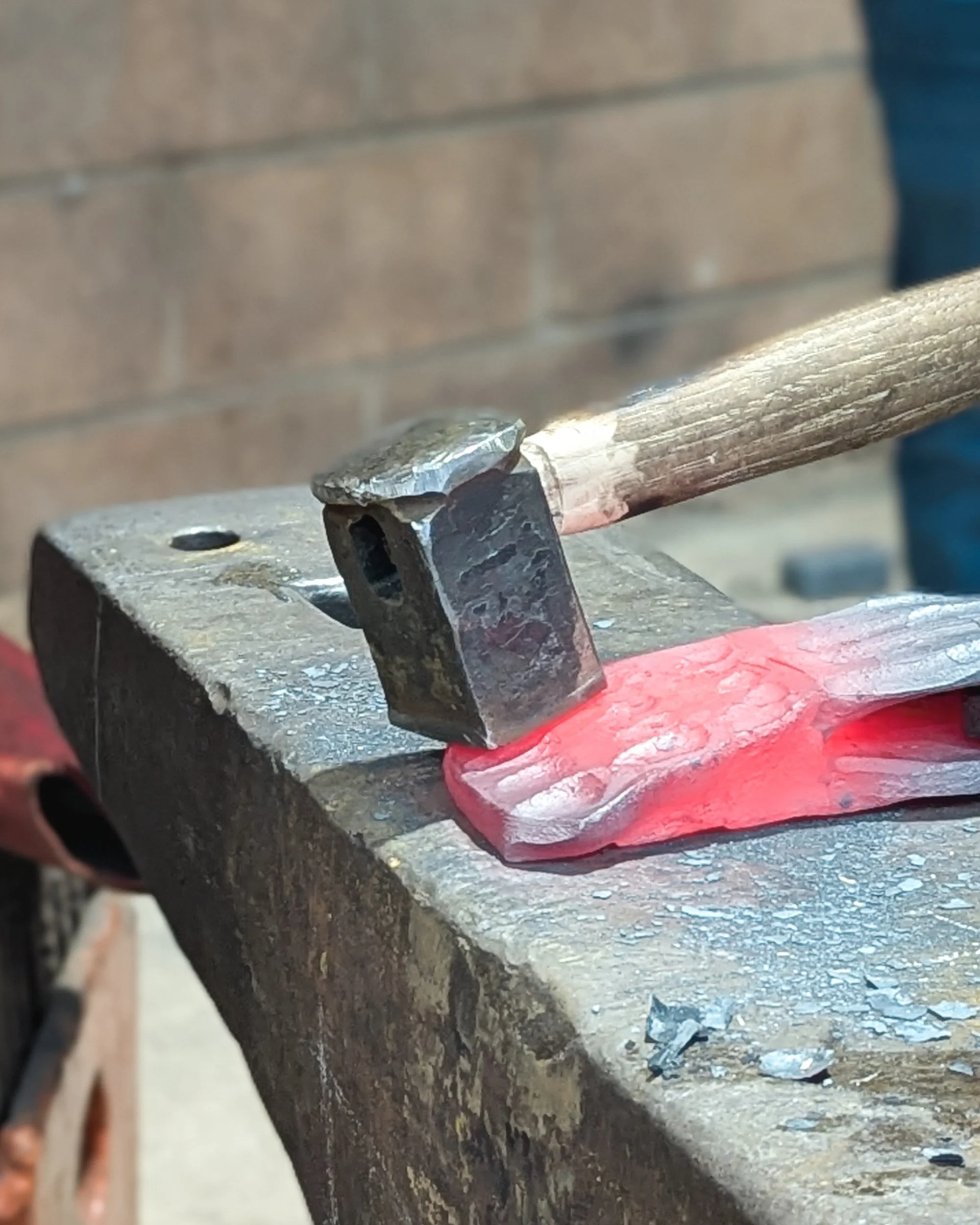A macro close-up of a steel shaping tool held precisely in place against glowing hot, dimpled metal, awaiting the next hammer blow to refine the design at Oldfield Forge.
