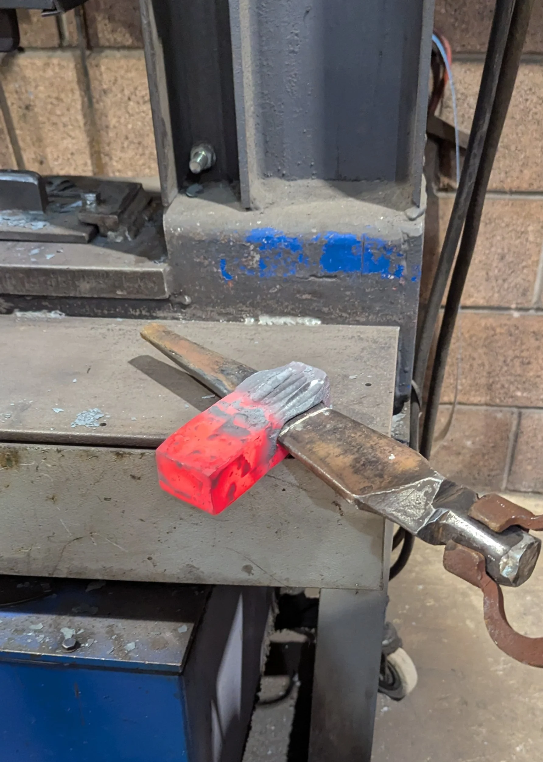 A steel billet recently removed from the hydraulic press at Oldfield Forge, showing a striking contrast between the glowing orange heated end and the dull grey cooled section.