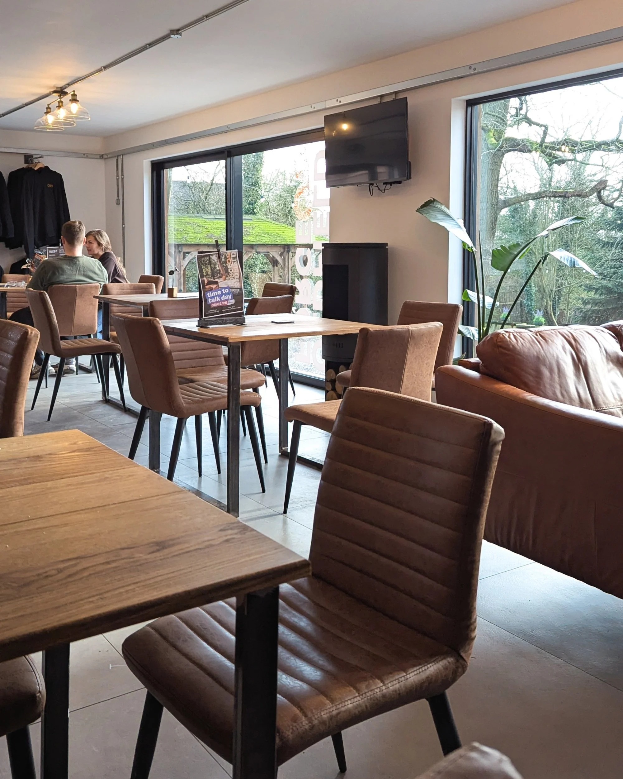 An overview of the modern and minimal cafe at Oldfield Forge, featuring comfortable tan leather chairs, wooden tables, indoor plants, and a clean, contemporary design.