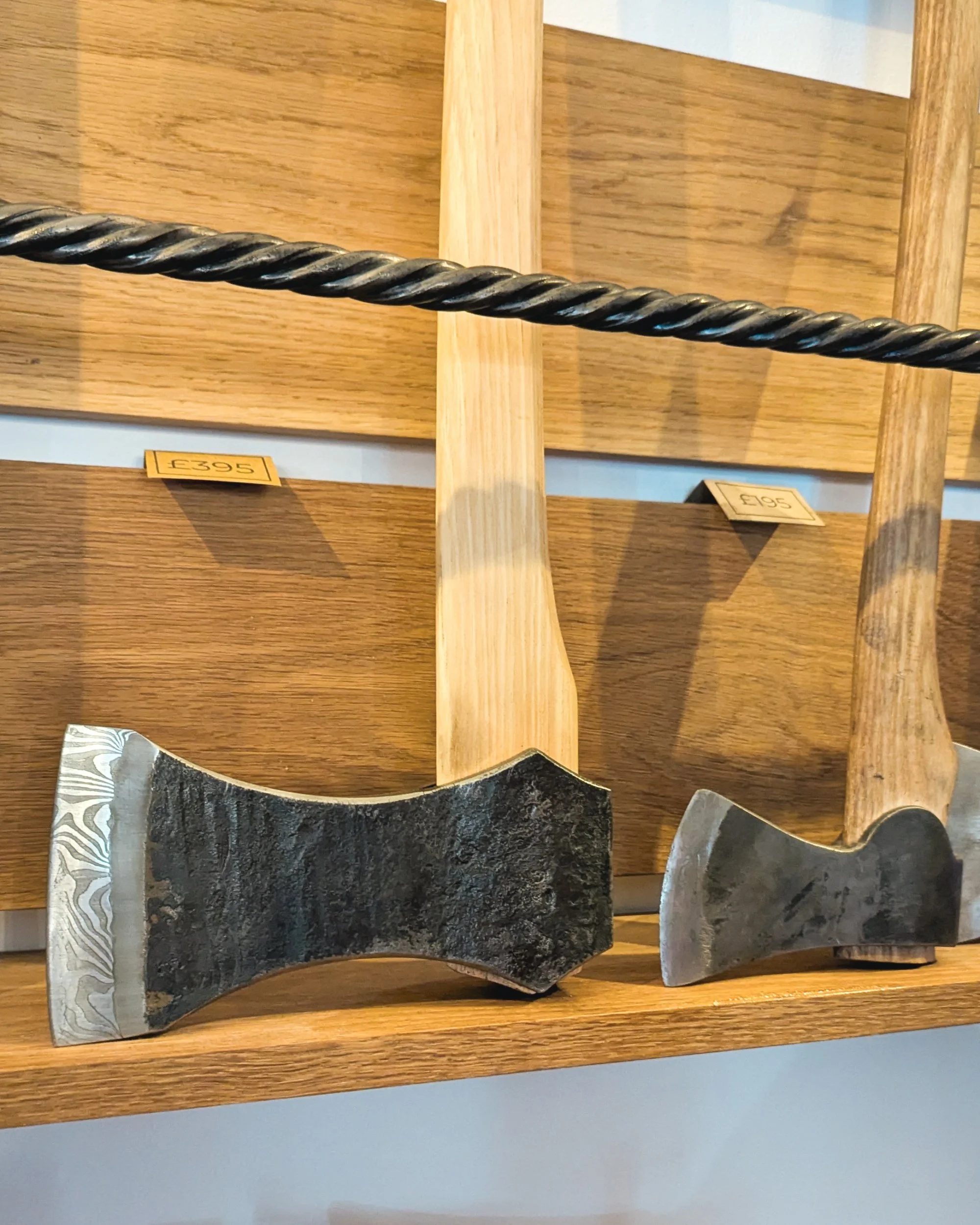 A close-up view of several completed, hand-forged axes for sale, showing the unique textures of the forged steel and the polished wood handles.