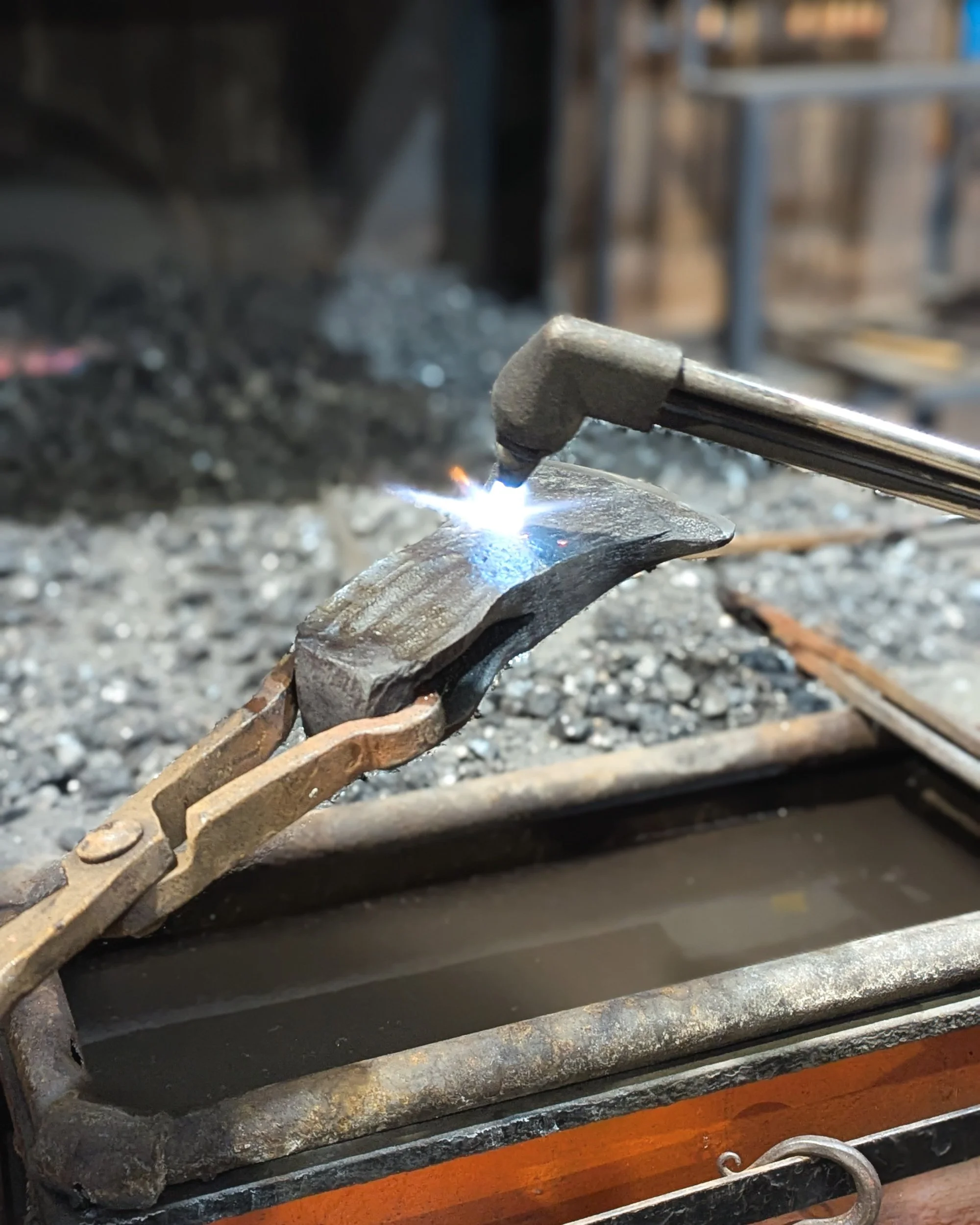 Using a gas torch to temper a hardened axe head, ensuring the tool is durable enough to withstand heavy use without chipping.