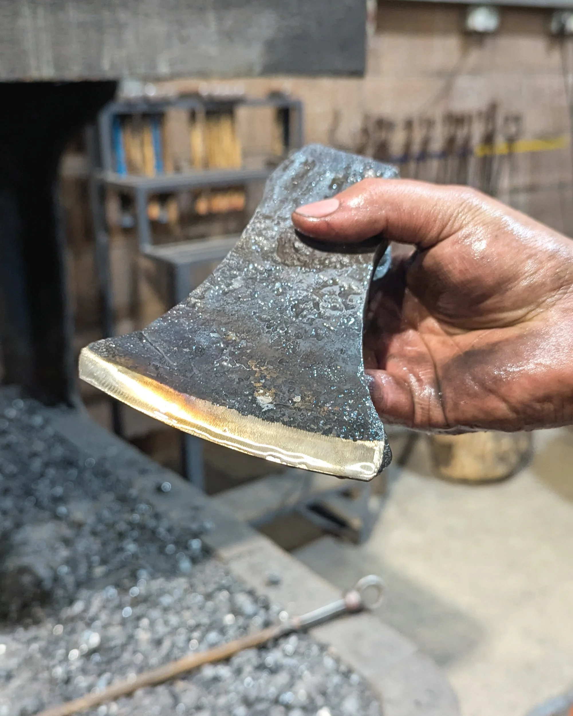 A hand holding a successfully tempered axe head, showing the distinct straw and orange oxide colors on the polished steel that indicate the perfect balance of hardness and toughness.