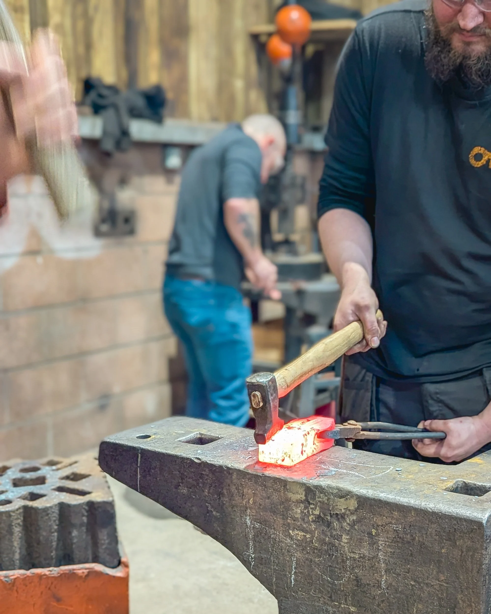 A motion-blurred action shot at Oldfield Forge capturing the powerful swing and energy of a blacksmith’s hammer striking a tool onto hot metal.