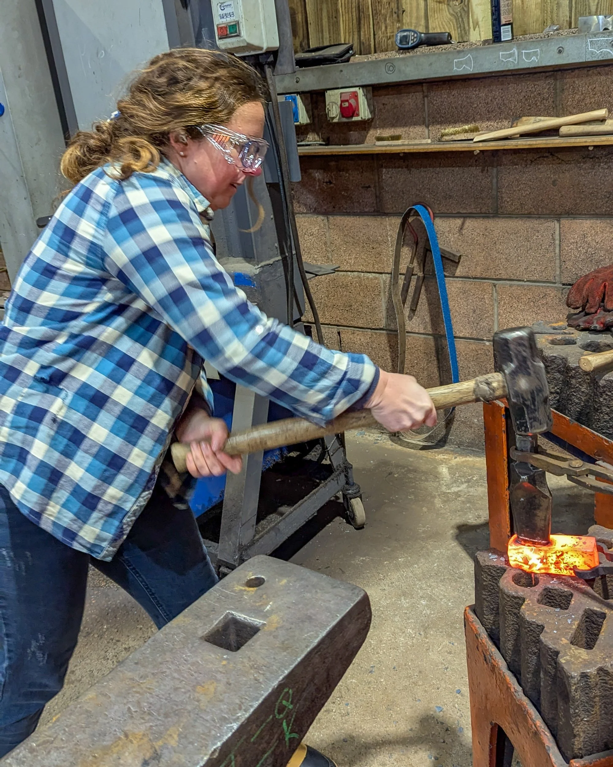 A blacksmith hammering a steel drift into a glowing axe head until it reaches the marked white line, ensuring the eye is the perfect size for the handle.