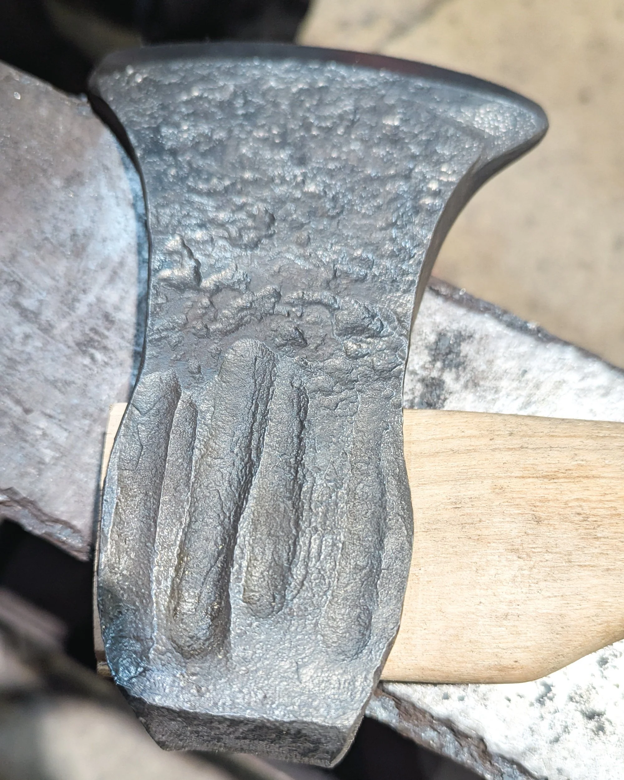 Close-up of the decorative and identifying marks stamped into the side of a hand-forged steel axe head.