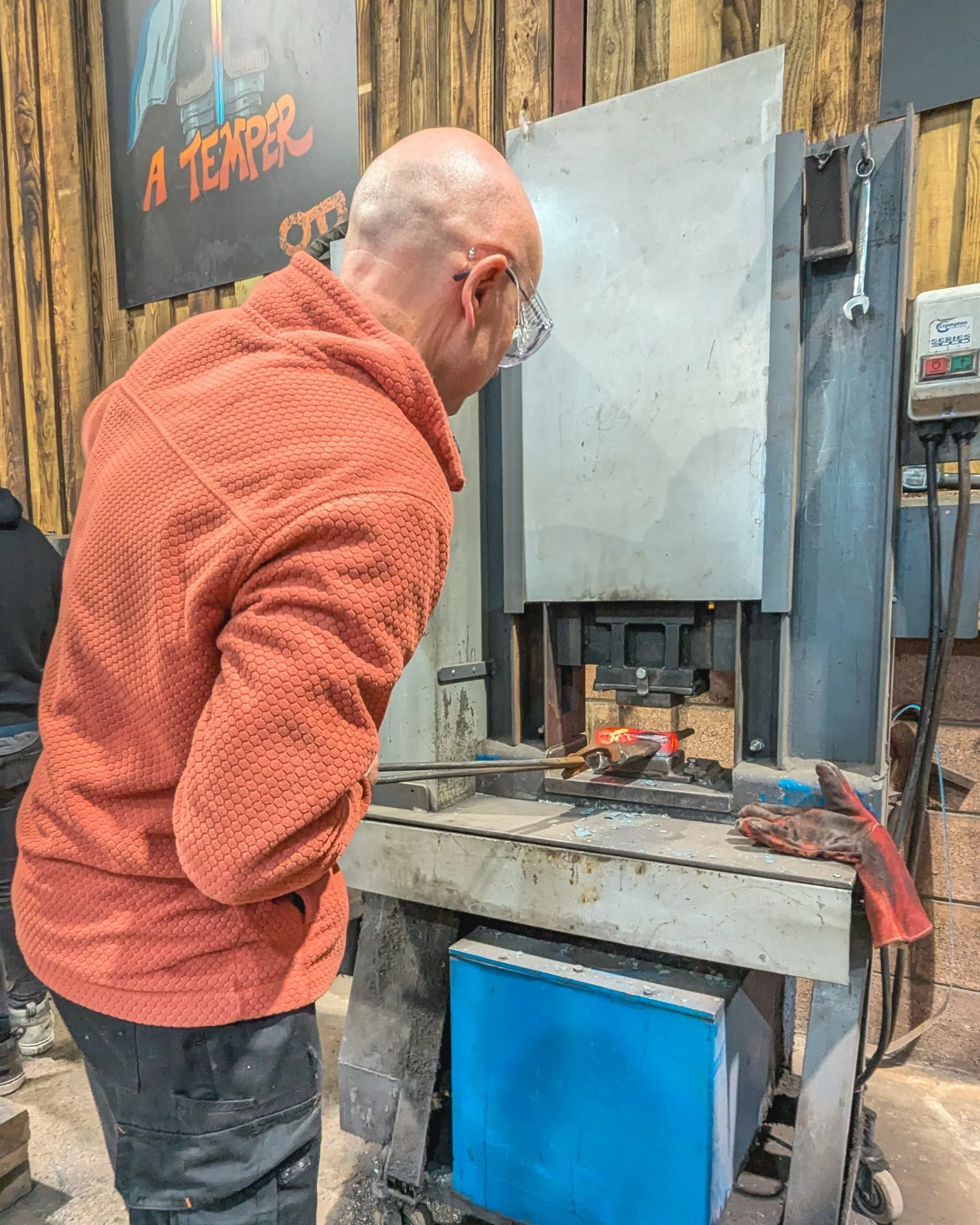 A powerful hydraulic forging press at Oldfield Forge clamping down on a glowing orange steel billet to compress and shape the metal with extreme pressure.