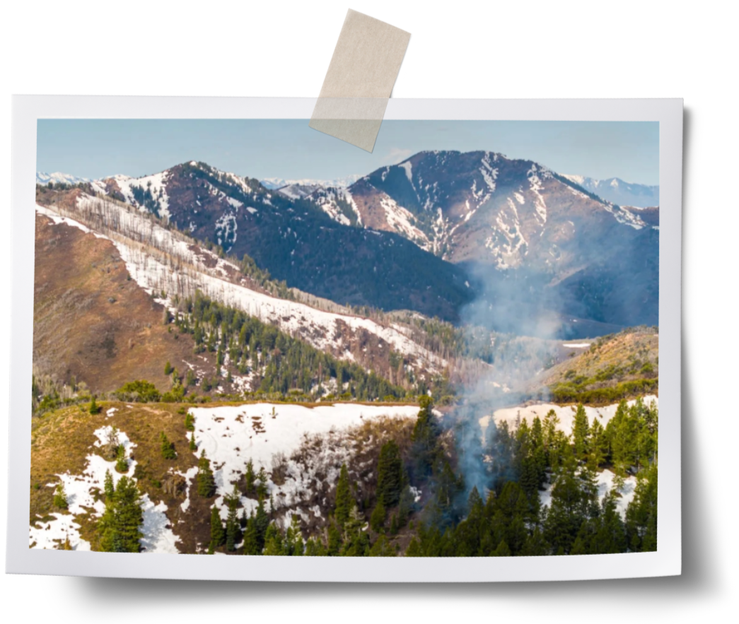 scotch tape holding up photo of mountain landscape with light smoke rising in the bottom right out of the trees