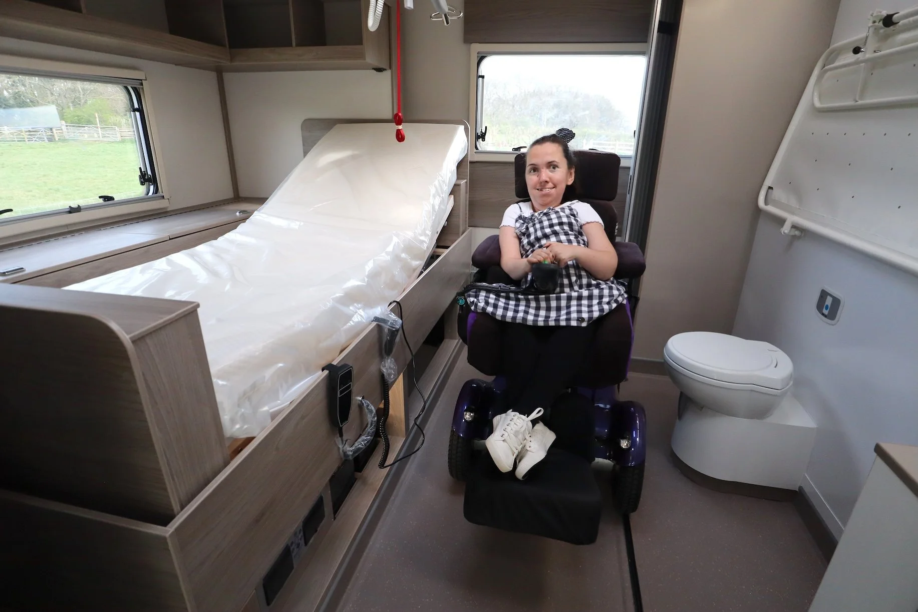  Karla, sitting in her powerchair at the back of a wheelchair accessible motorhome, between a profiling bed and the washroom 