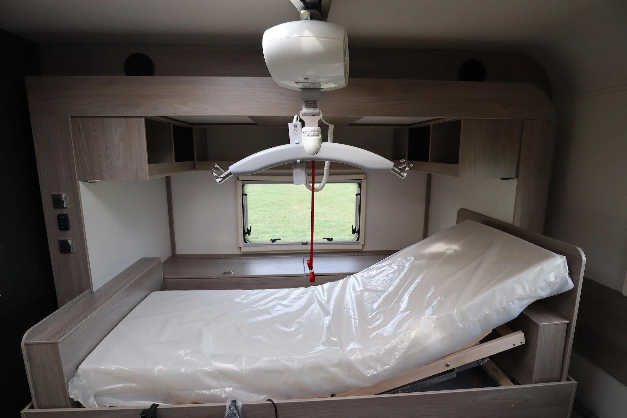  The side view of a single profiling bed in a wheelchair accessible motorhome. There is a ceiling-track hoist hanging above it 