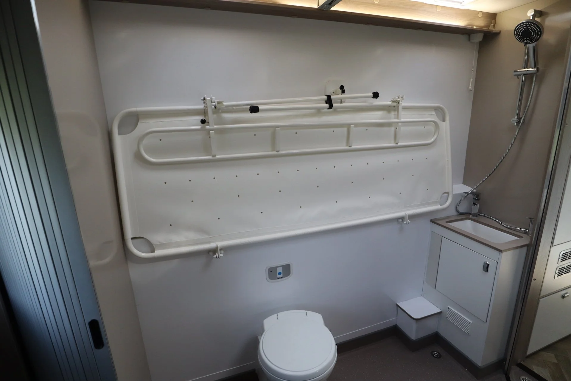  A modified washroom in a disabled accessible motorhome. Above the toilet is a fold-down shower bed in its stowed position.  