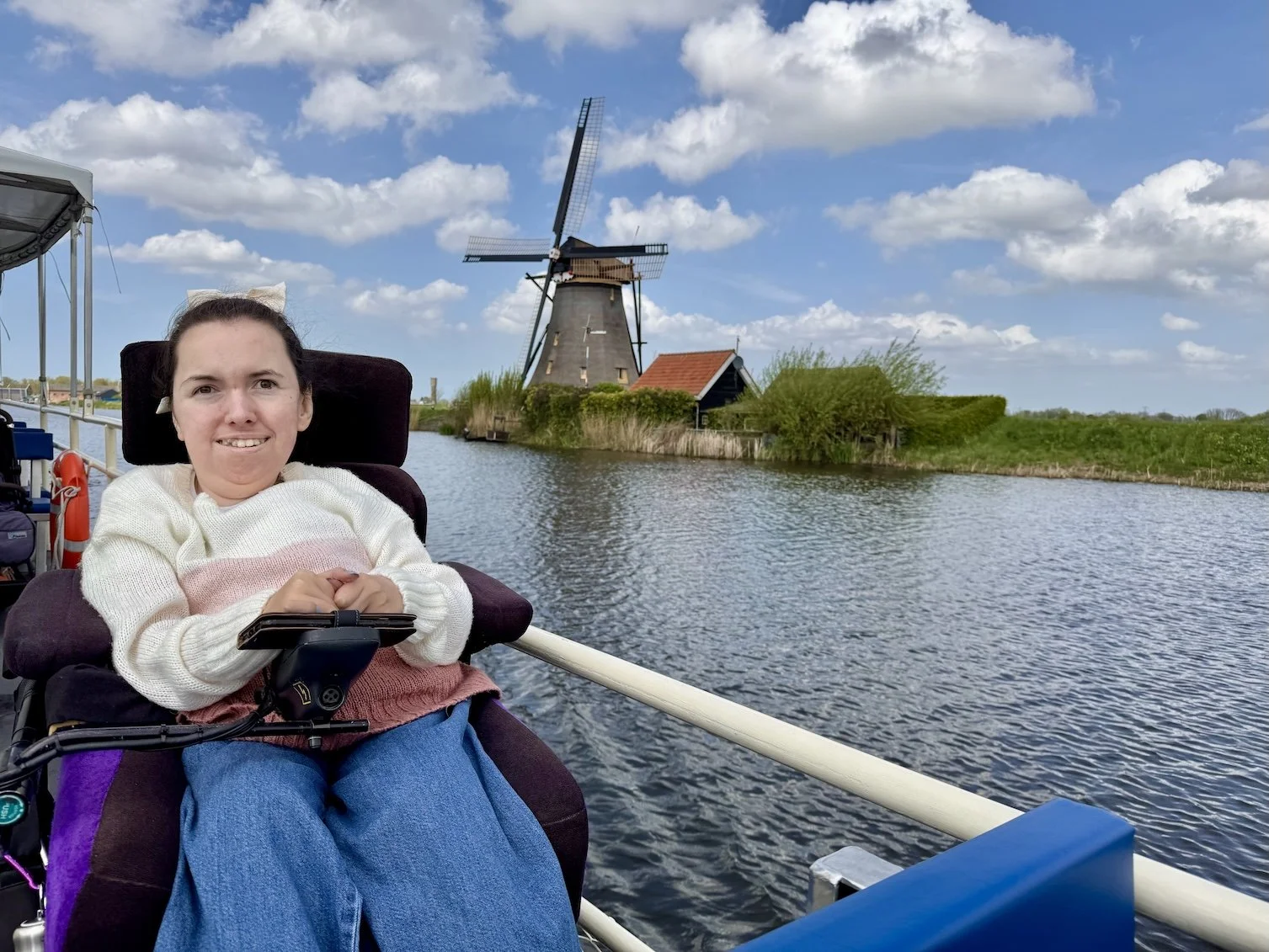  Karla in her Balder electric wheelchair on a boat at Werelderfgoed Kinderdijk in the Netherlands. A traditional Dutch windmill is behind her 