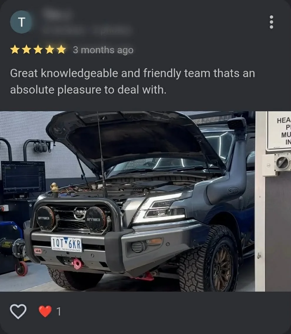 A silver off-road vehicle with its hood open, equipped with a bull bar, two large off-road lights, a snorkel, large tires, and a visible license plate, inside a workshop or garage.