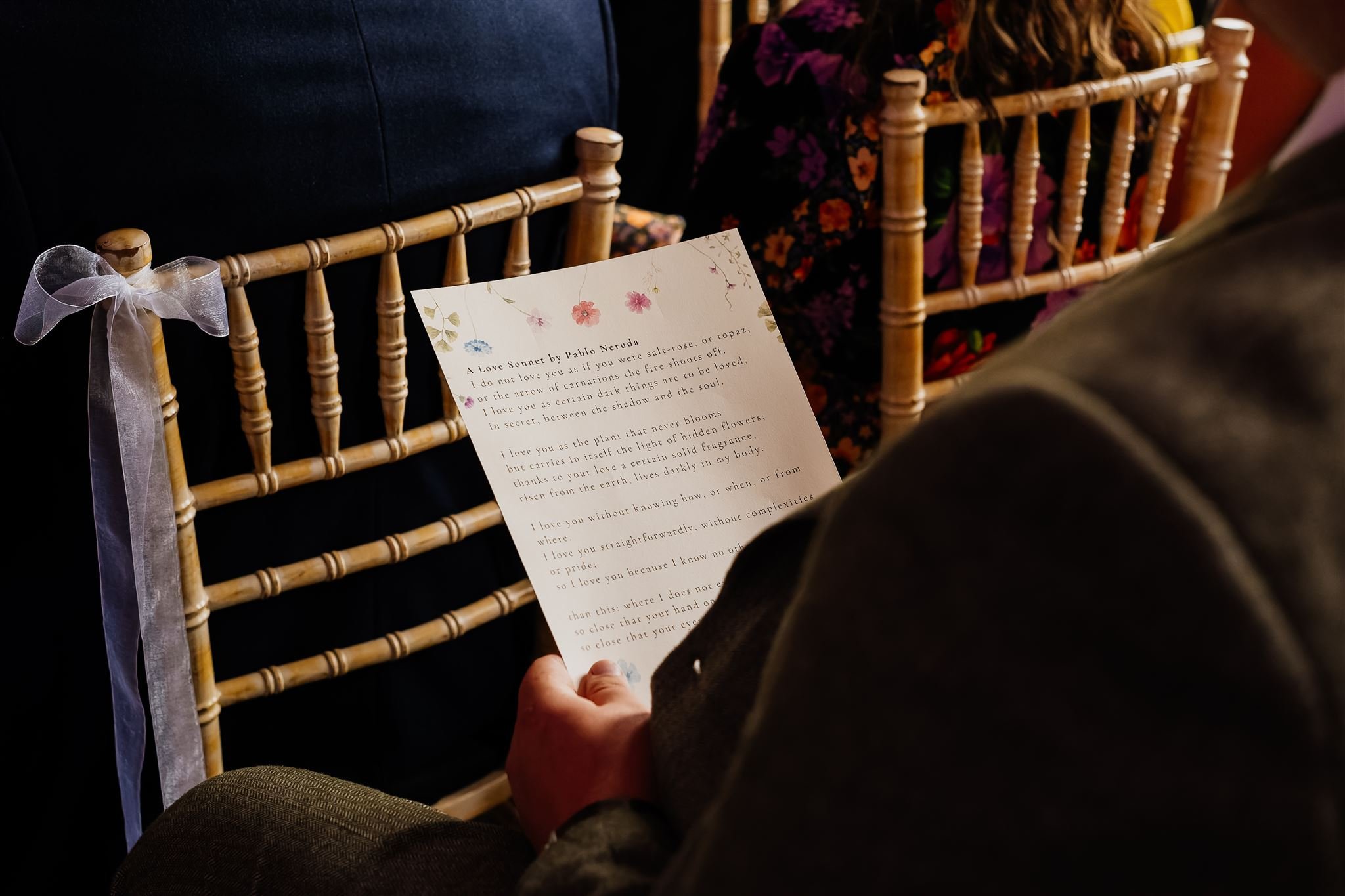 A close up of a beautifully printed wedding reading card in a man's hands, at a wedding.