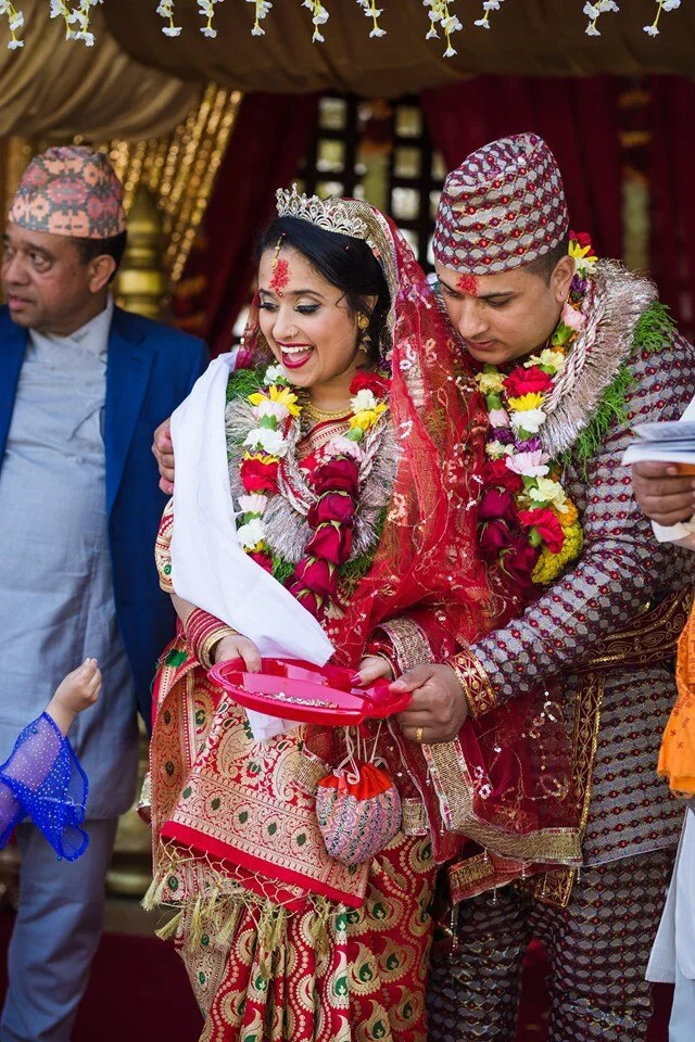 A traditional Nepali wedding ceremony with the bride and groom dressed in colorful, ornate attire, exchanging rings and floral garlands, surrounded by family members in a decorated setting.