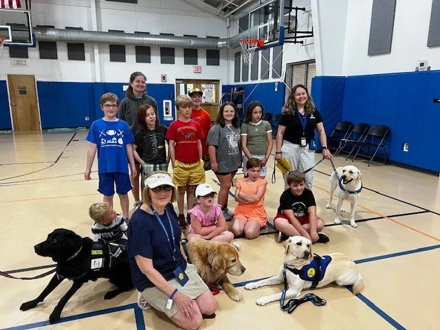 Group of children and adults in a gymnasium with therapy dogs.