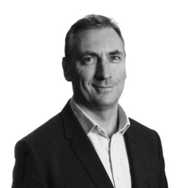 A black-and-white professional headshot of a man in a suit, smiling slightly.
