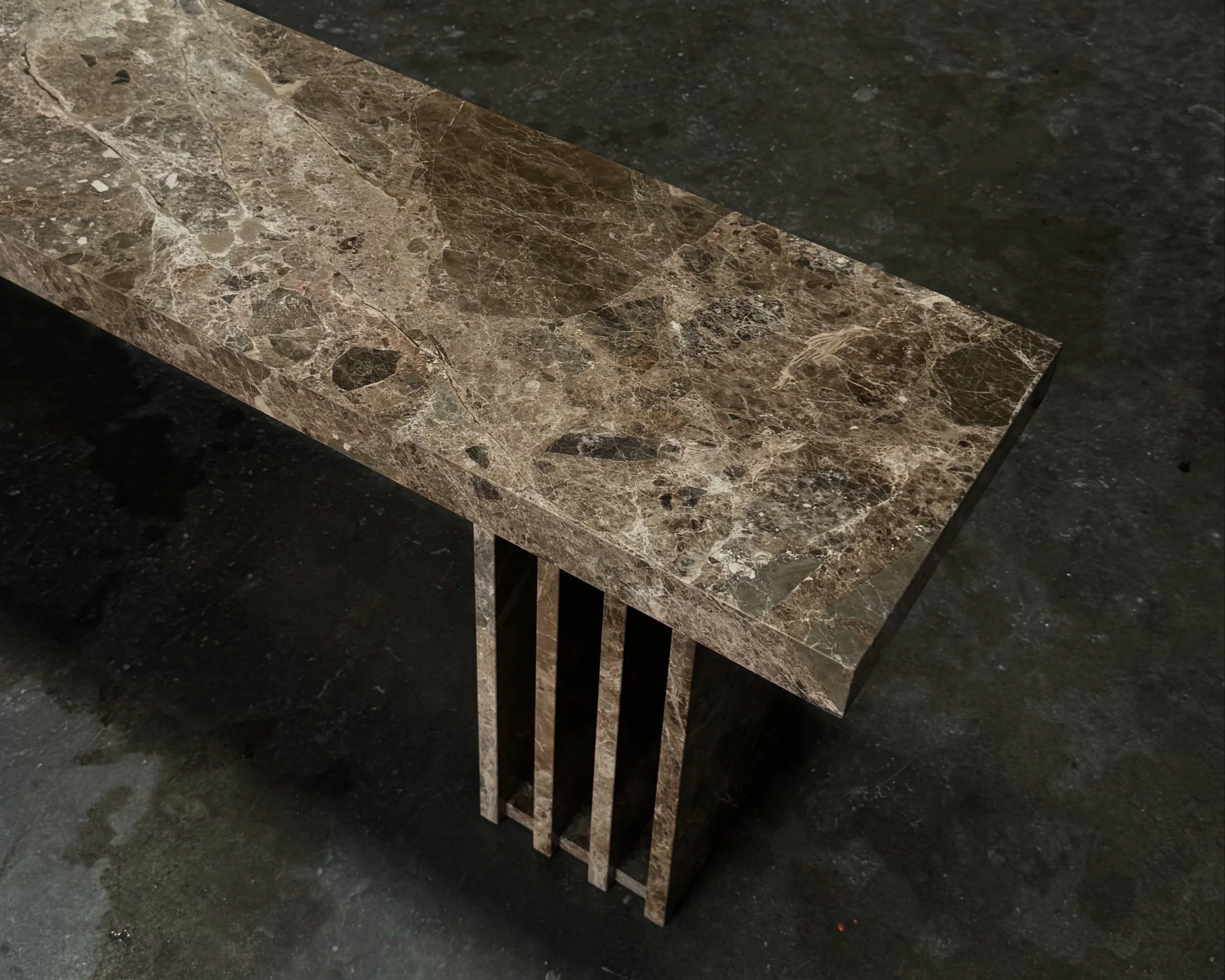 Emperador marble bench featuring vertical slats, placed on a dark, textured floor.