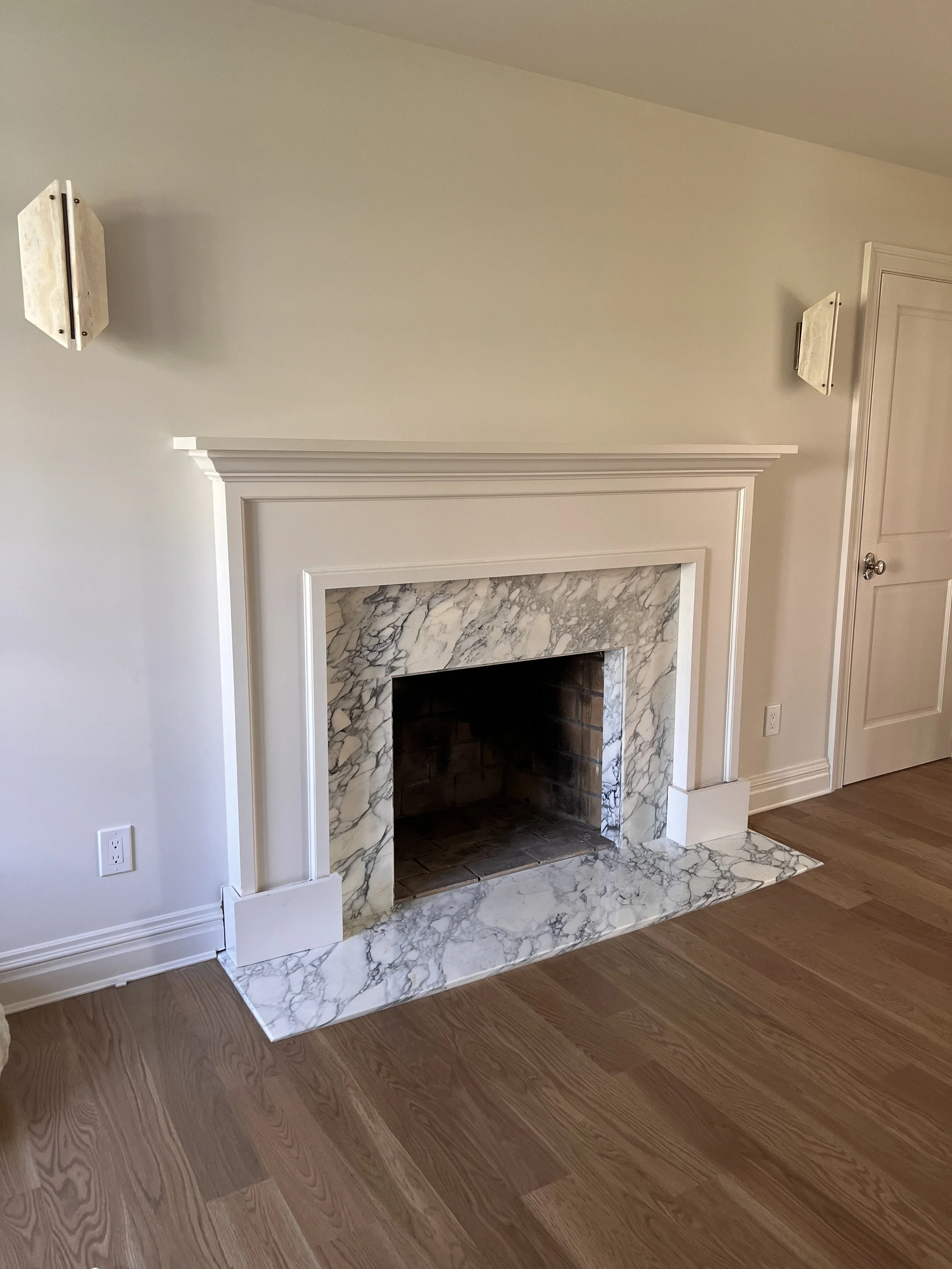Living room with a custom Arabescato Turqouise fireplace, hardwood floors, and two wall-mounted light fixtures in Roslyn, New York. 