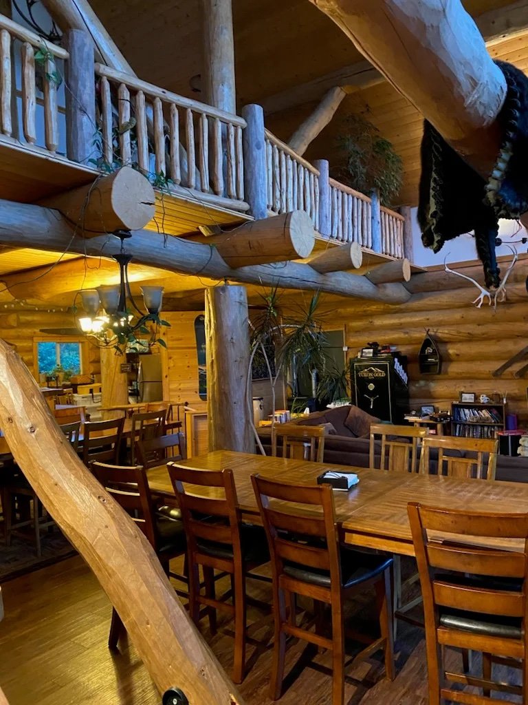 Cozy log cabin interior with wooden furniture, dining table, and loft area.