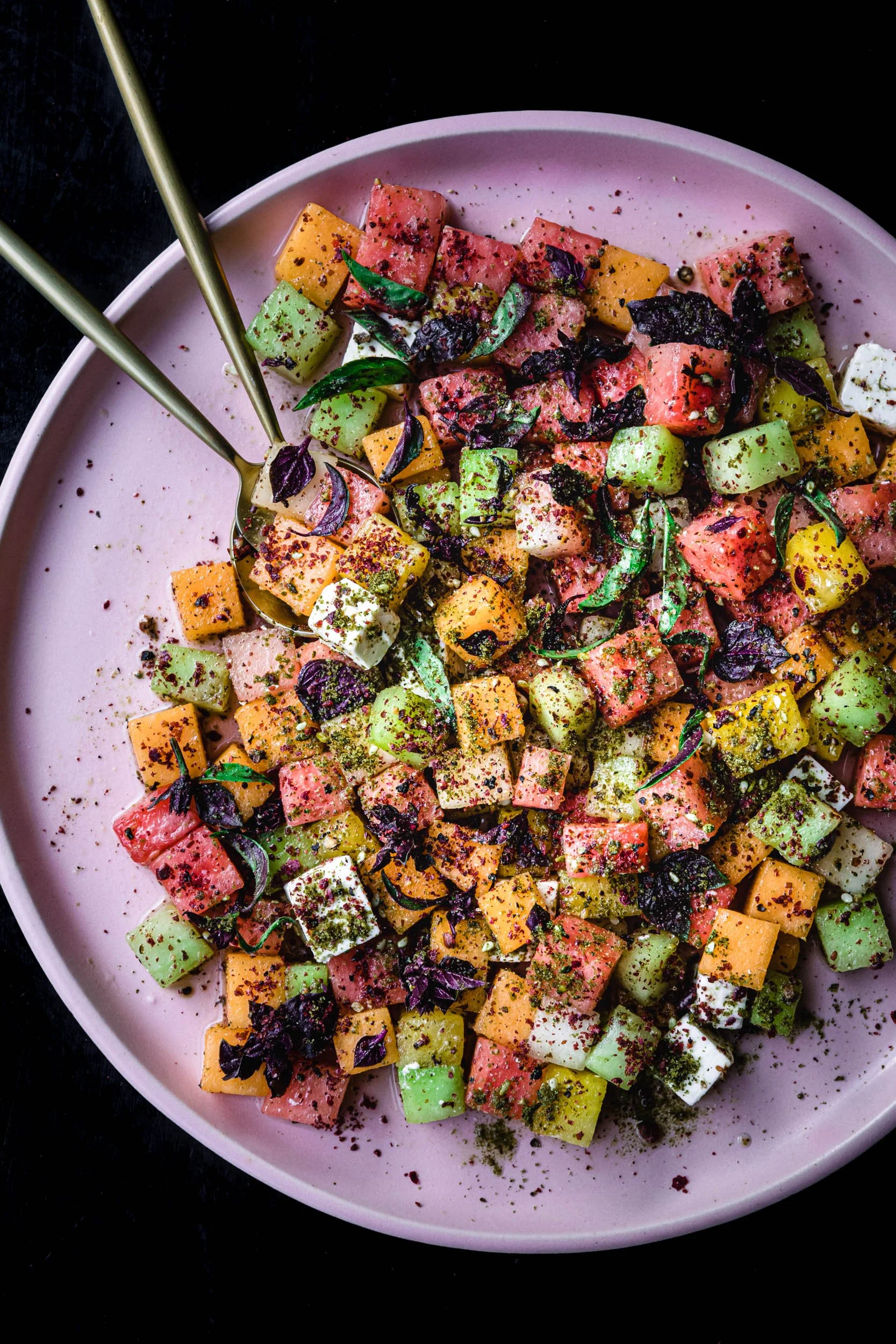 Watermelon and feta salad with basil on a pink plate and black background. 