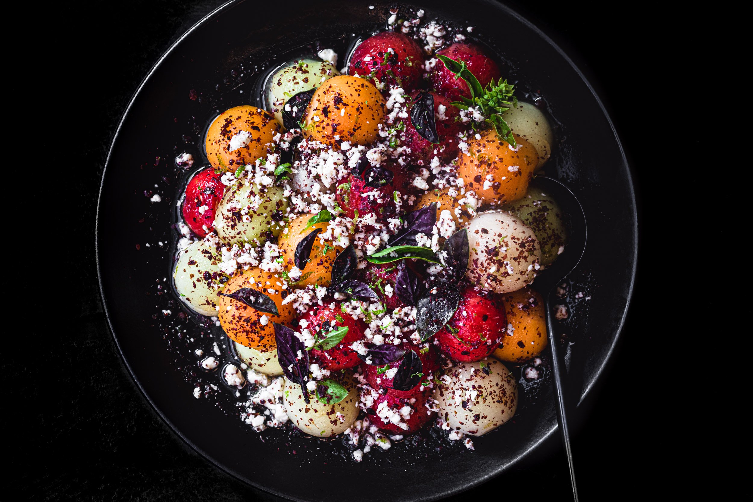 Colorful melon salad on a black plate with feta and basil and a black background