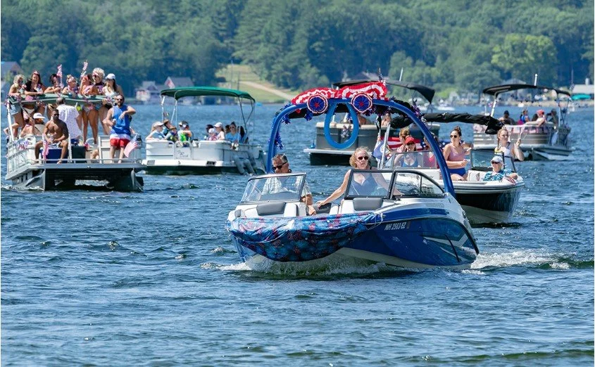 Multiple boats on the water during a summer gathering, with people enjoying the sunny day and dancing on a boat.